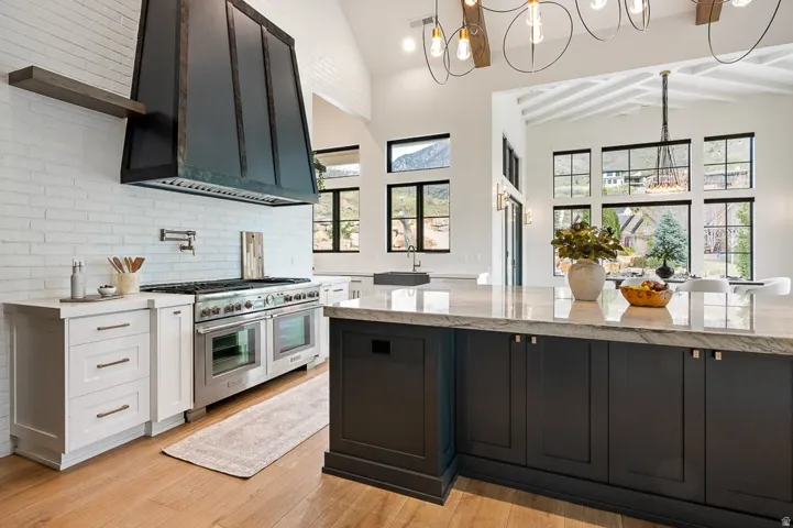 Kitchen with hanging lights, two tone color scheme, range with two ovens, light stone counters, and lofted ceiling