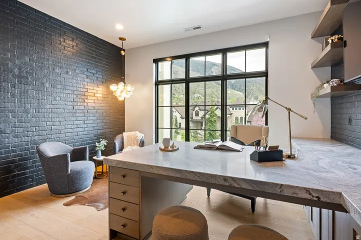 Office space with brick wall, an accent wall, hanging lights, and light wood-style flooring