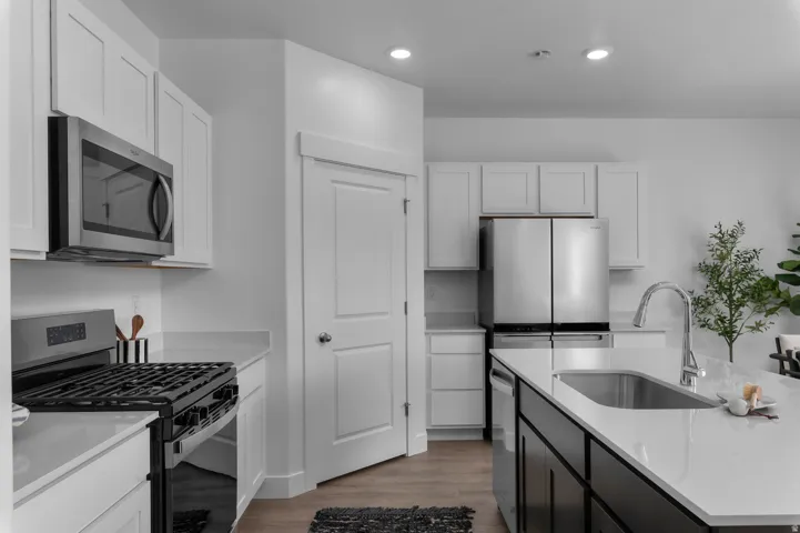 Two tone kitchen featuring stainless steel appliances, two tone cabinetry, light wood-style flooring, light stone counters, and a kitchen island with sink