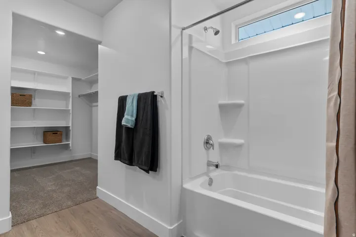 Bathroom with light wood-style flooring, a walk in closet, and shower / bathtub combination with curtain