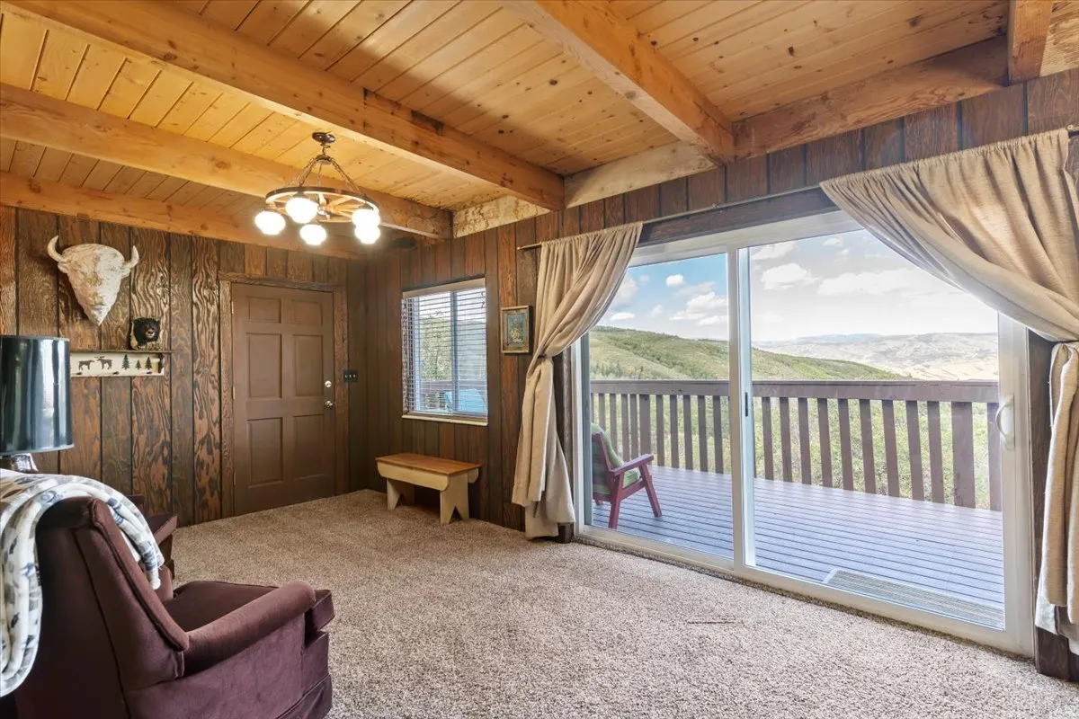 Living room featuring hanging lights, a mountain view, carpet floors, wooden walls, and a wooden ceiling with exposed beams