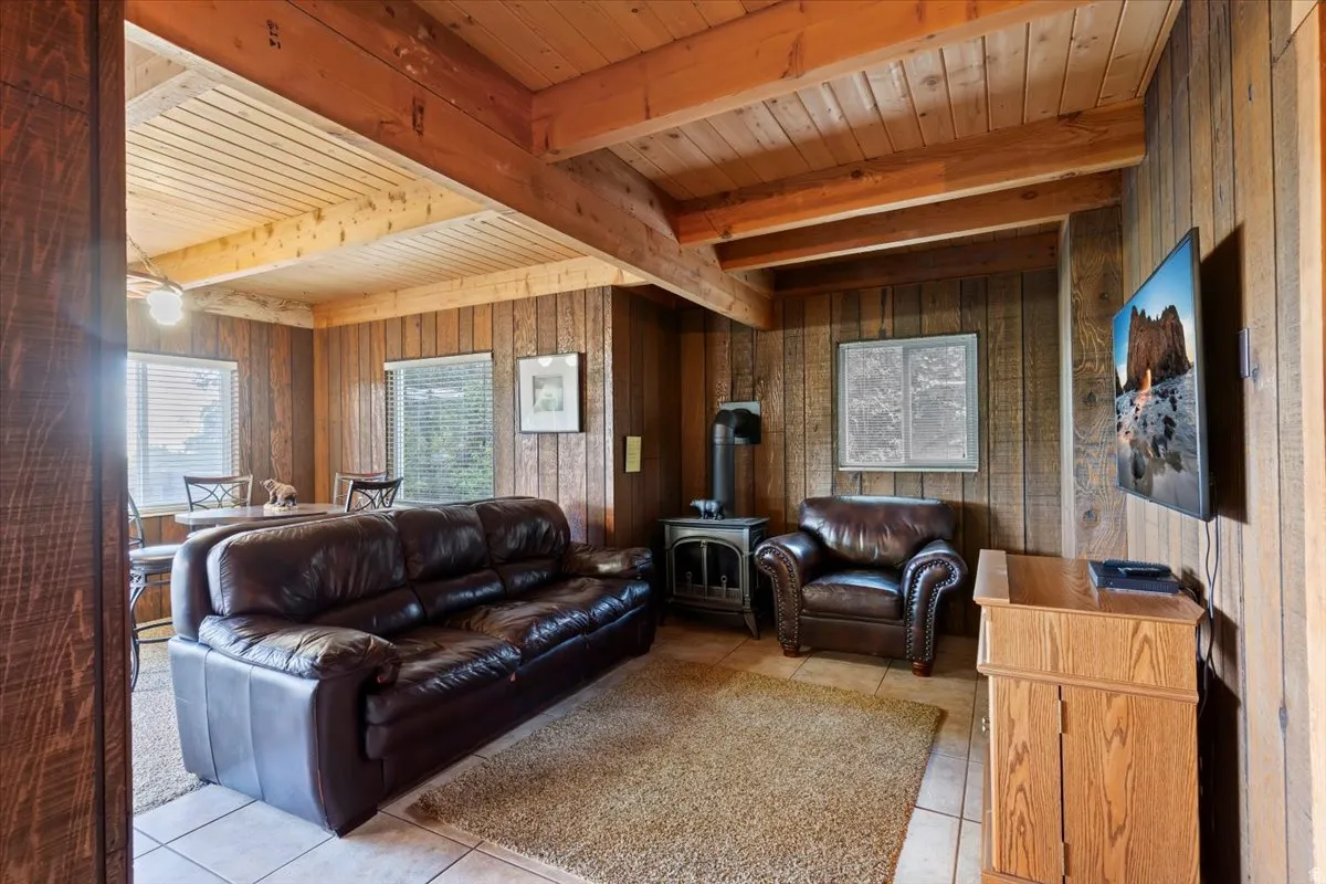 Living area featuring a wood stove, wooden walls, light tile patterned floors, and a wooden ceiling with exposed beams