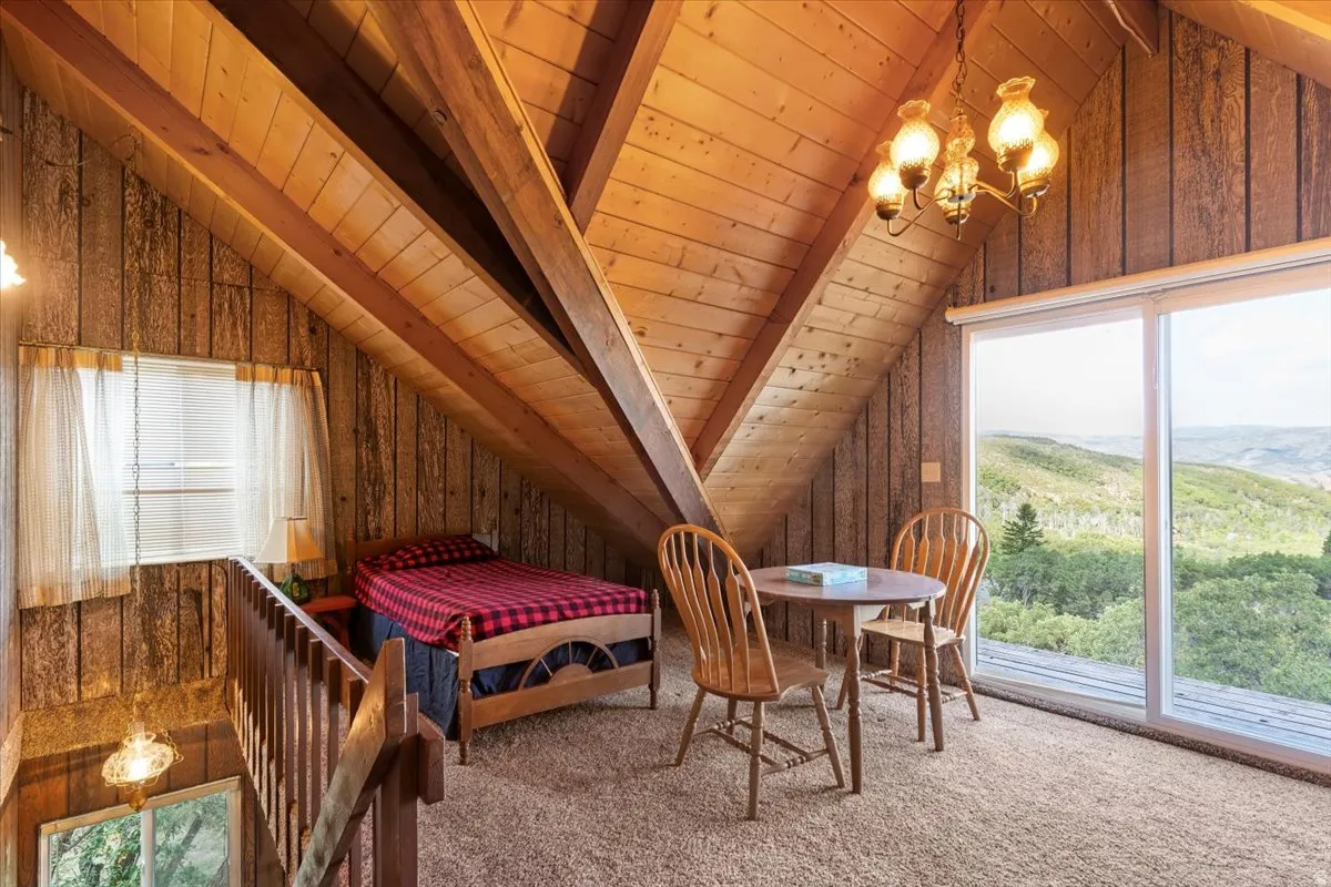 Carpeted  loft bedroom with vaulted ceiling with beams, wood ceiling, wooden walls, and suspended lighting