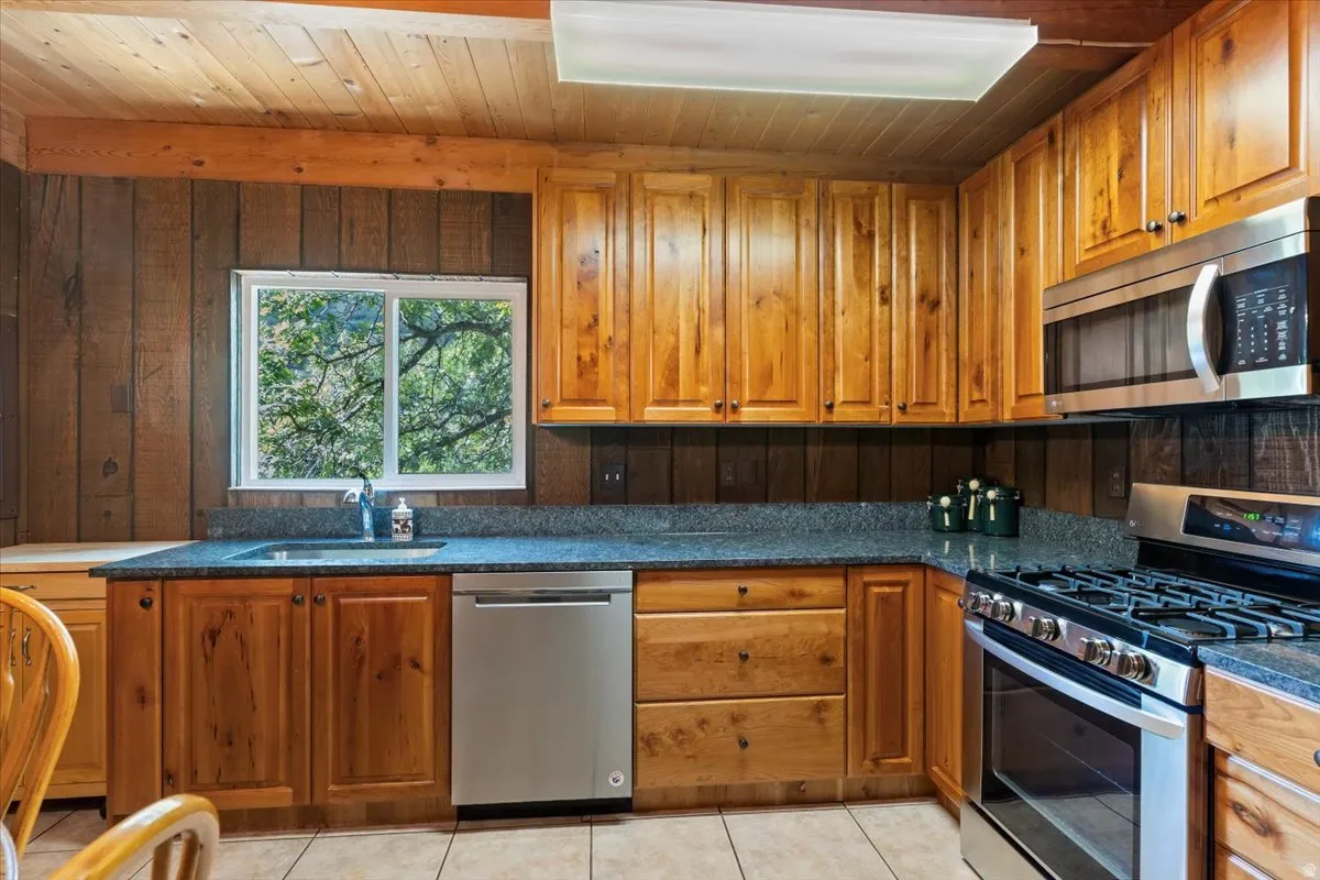 Kitchen featuring stainless steel appliances, wood finish cabinets, wood ceiling, light tile-patterned flooring.