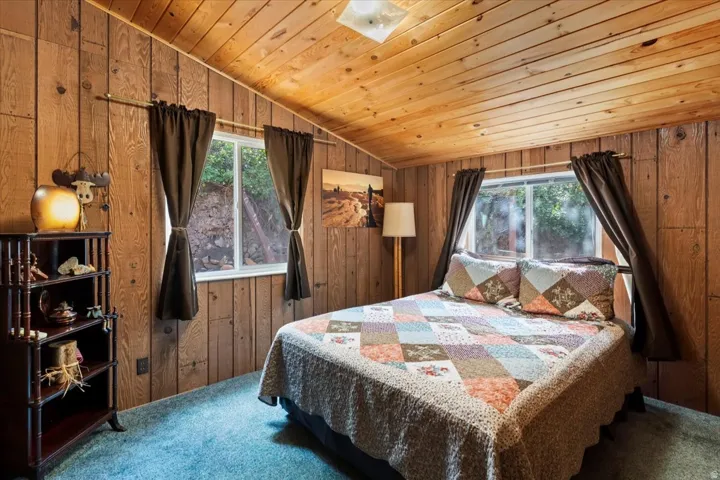 Bedroom with carpet floors, wooden walls, and a vaulted wooden ceiling