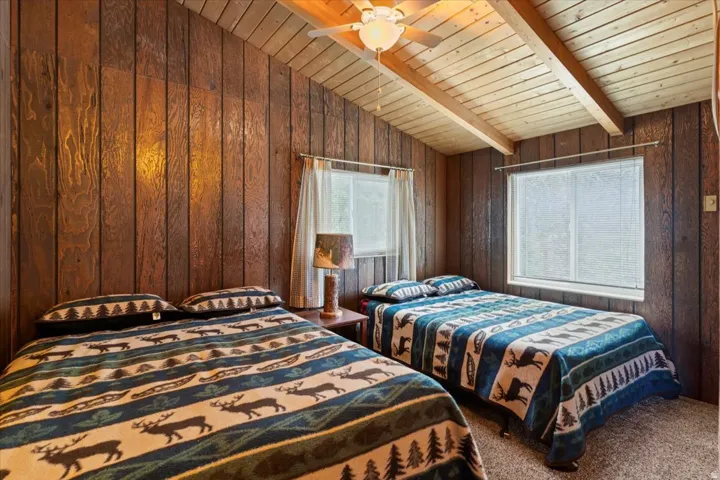 Carpeted bedroom with vaulted ceiling with beams, wood walls, and wooden ceiling