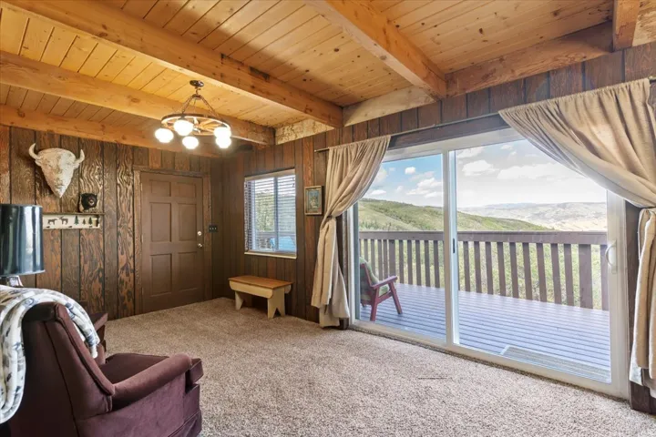Living room featuring hanging lights, a mountain view, carpet floors, wooden walls, and a wooden ceiling with exposed beams