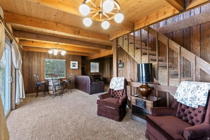 Living room featuring a chandelier, carpet floors, wood walls, and a wood ceiling with exposed beams