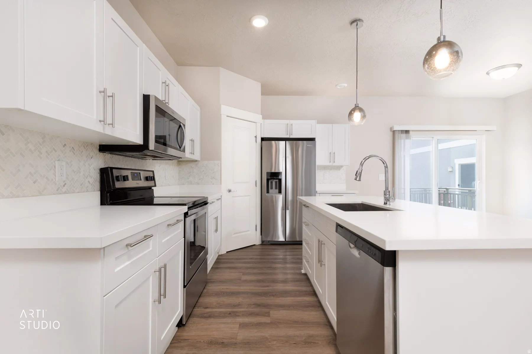 Kitchen with stainless steel appliances, a center island with sink, white cabinets, hanging light fixtures, and dark wood-style flooring