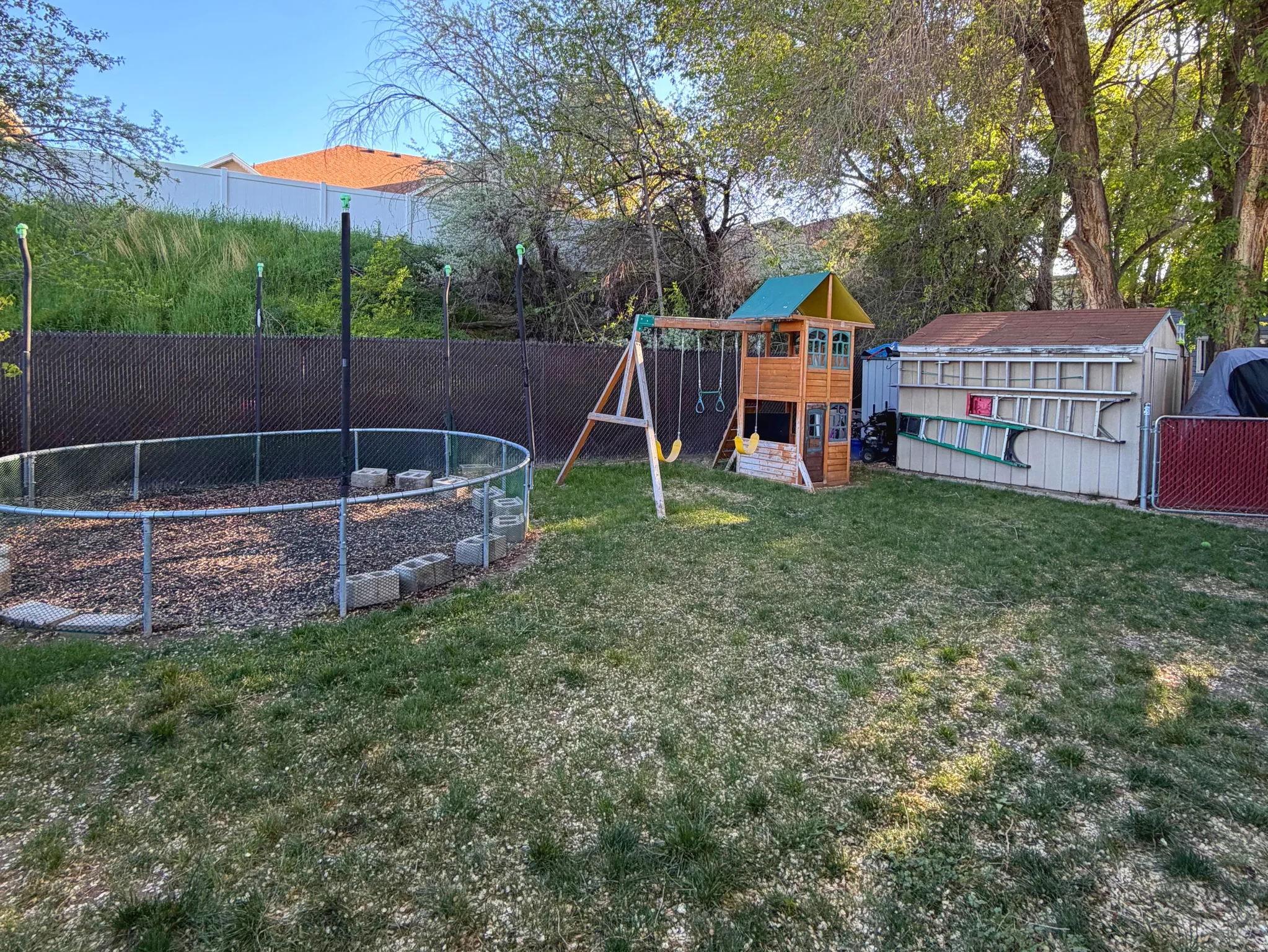 Fenced backyard featuring a playground, a trampoline, and an outbuilding