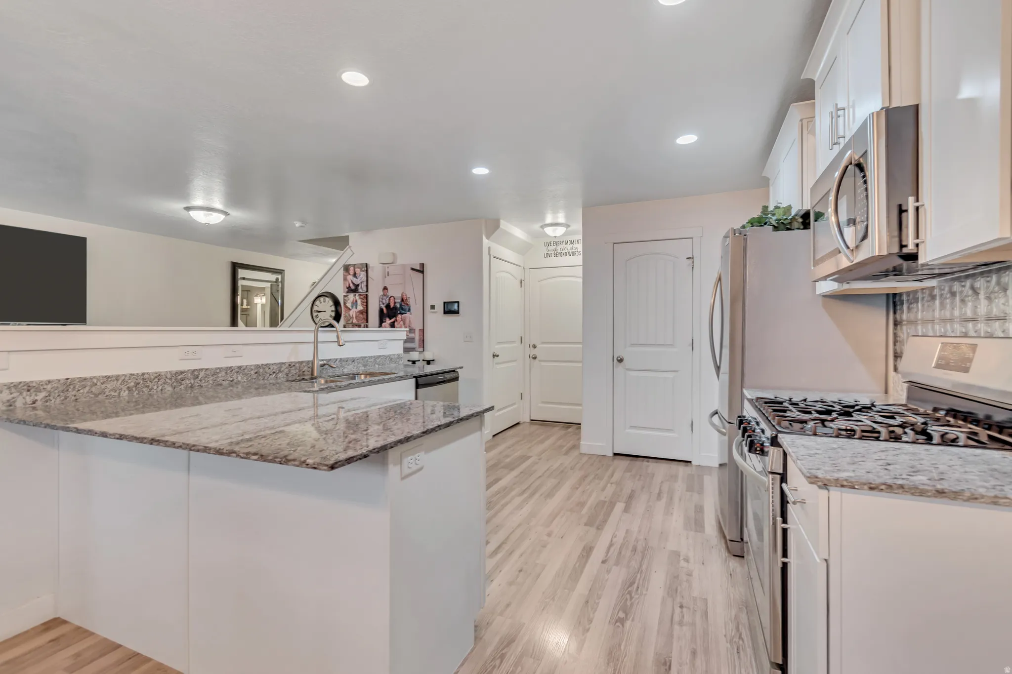 Kitchen featuring stainless steel appliances, light stone counters, light wood-style floors, white cabinetry, and recessed lighting