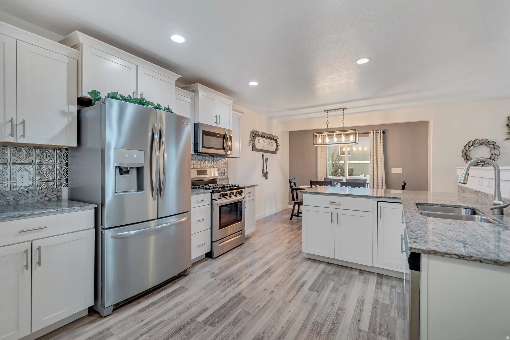 Kitchen featuring stainless steel appliances, light stone countertops, white cabinets, and light wood-type flooring