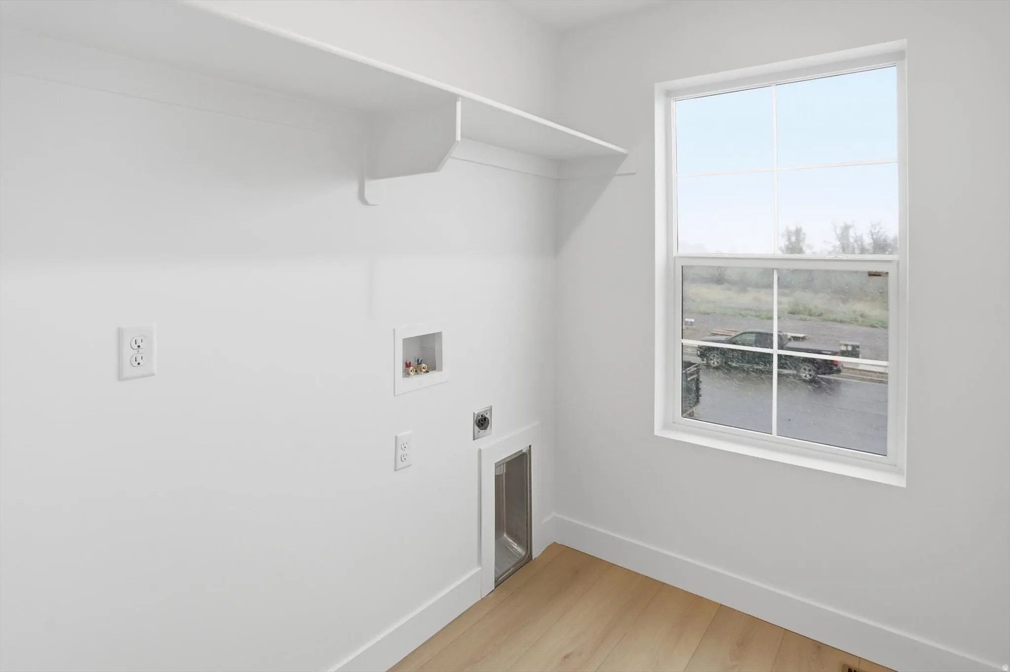 Laundry area with light wood-type flooring, hookup for an electric dryer, and hookup for a washing machine