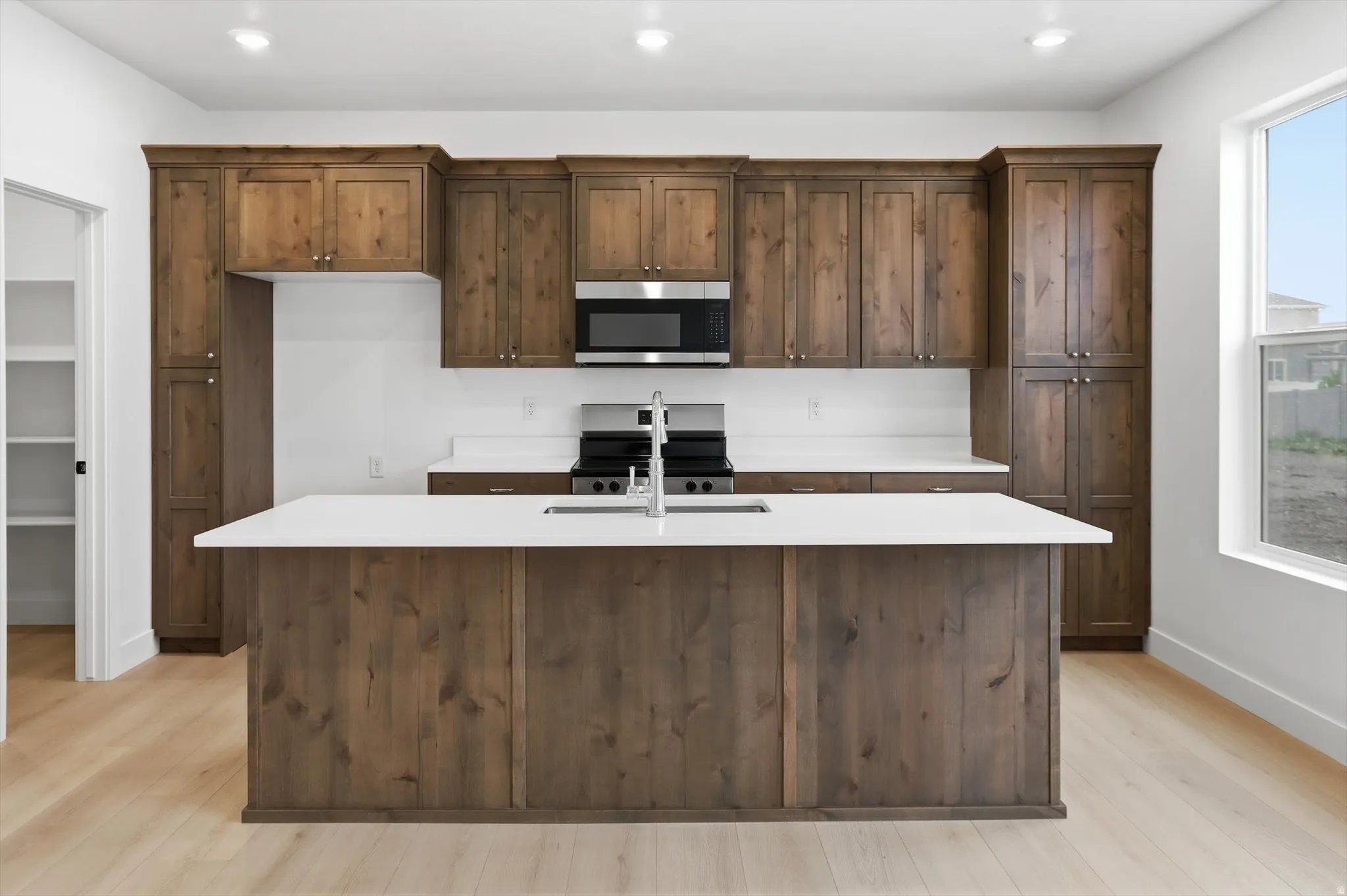 Kitchen featuring stainless steel appliances, a center island with sink, light stone counters, light wood-type flooring, and dark wood finish cabinets