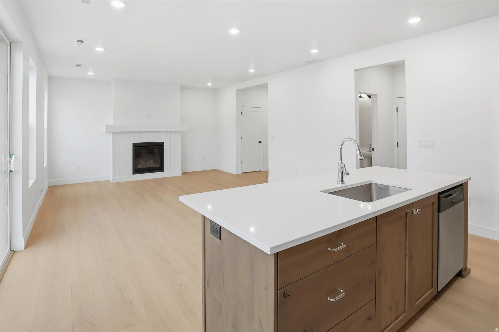 Kitchen with an island with sink, recessed lighting, a glass covered fireplace, open floor plan, and light wood-style flooring
