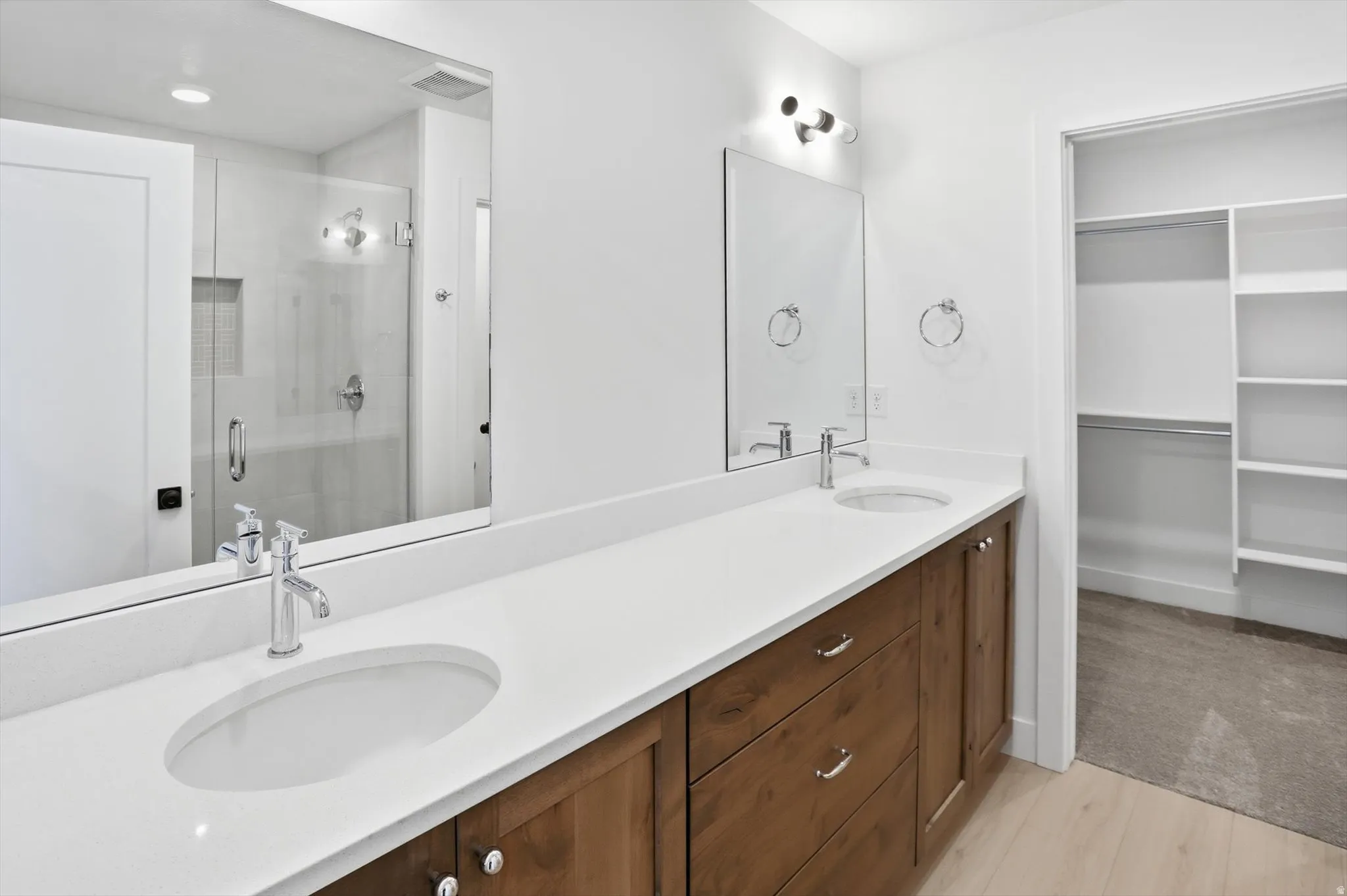 Bathroom with a spacious closet, double vanity, a shower stall, and light wood finished floors