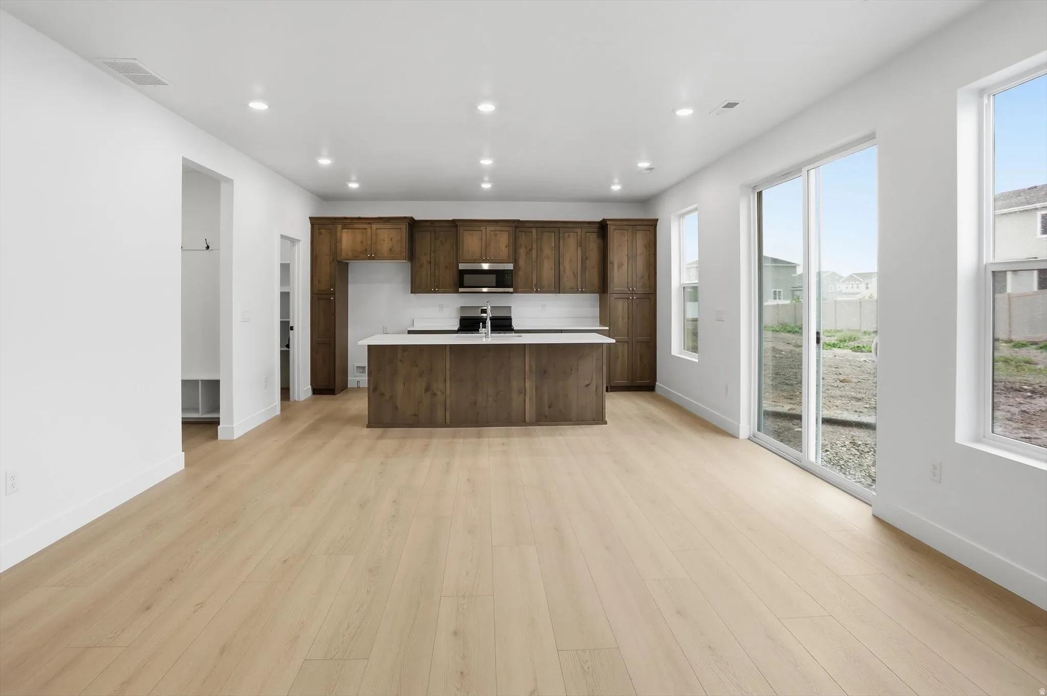 Kitchen with a center island with sink, light wood-type flooring, recessed lighting, stainless steel microwave, and open floor plan