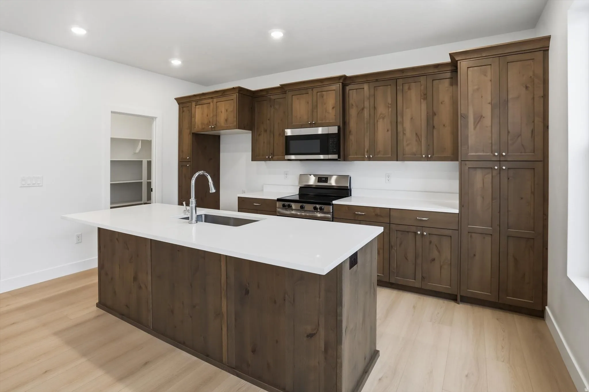 Kitchen featuring stainless steel appliances, light wood-style flooring, a kitchen island with sink, dark wood finish cabinets, and recessed lighting