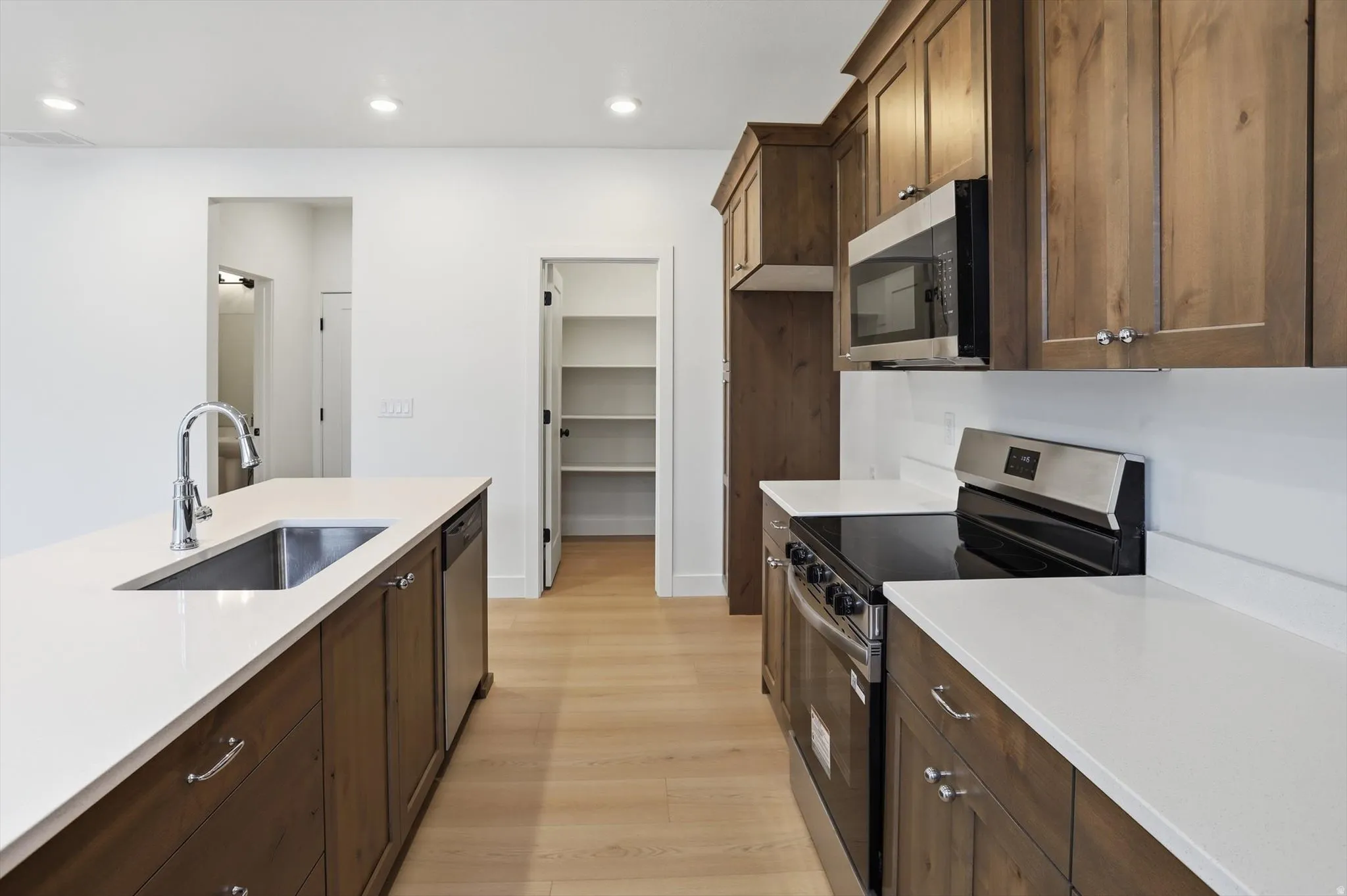 Kitchen with stainless steel appliances, light wood-type flooring, dark wood finish cabinetry, light stone countertops, and recessed lighting