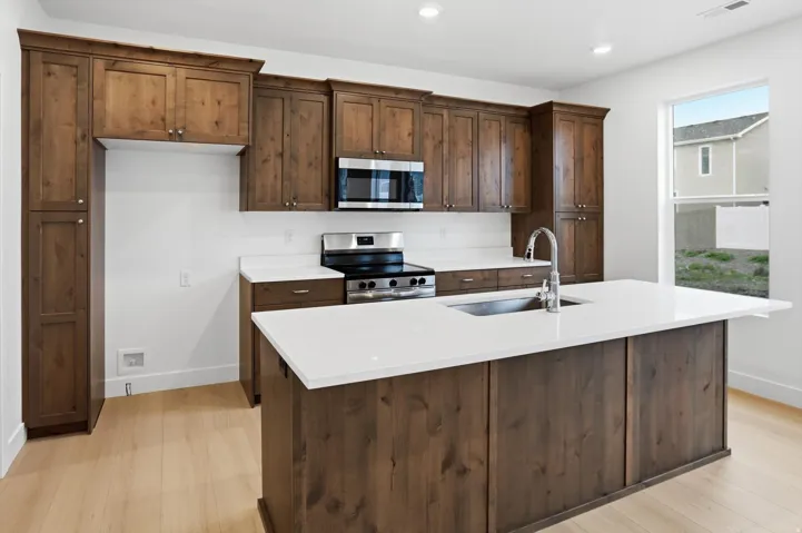 Kitchen featuring stainless steel appliances, dark wood finish cabinets, a center island with sink, light wood-style floors, and recessed lighting