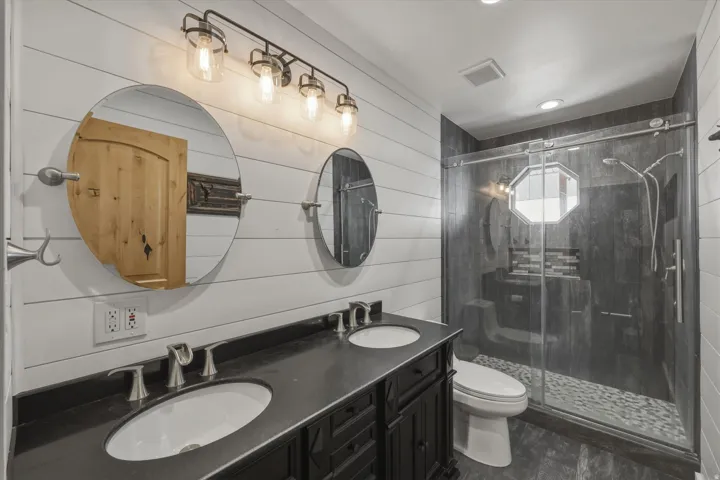 Full bathroom featuring double vanity, a stall shower, and wood walls