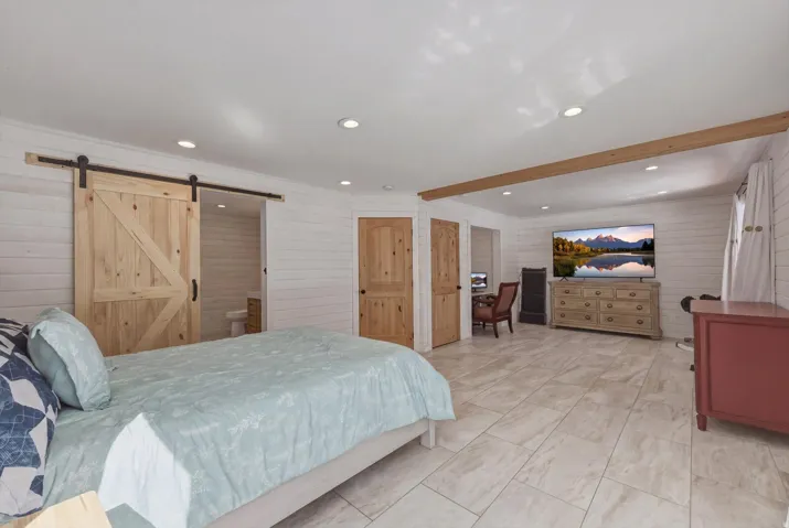 Bedroom with a barn door, recessed lighting, wooden walls, ensuite bathroom, and beam ceiling