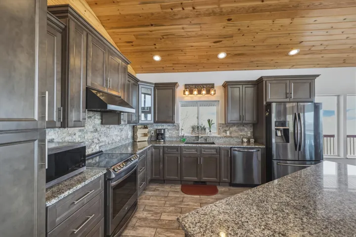 Kitchen with dark wood finish cabinets, stainless steel appliances, dark stone countertops, and recessed lighting