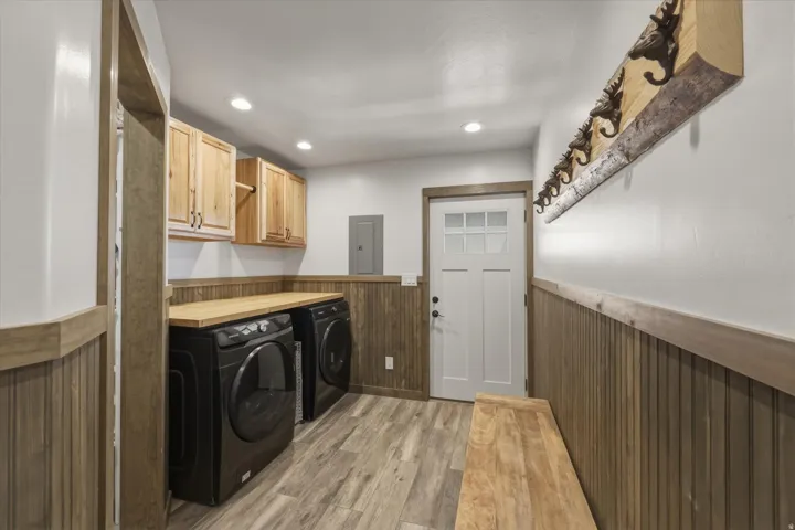 Laundry area featuring a wainscoted wall, cabinet space, light wood finished floors, wooden walls, and washer and dryer
