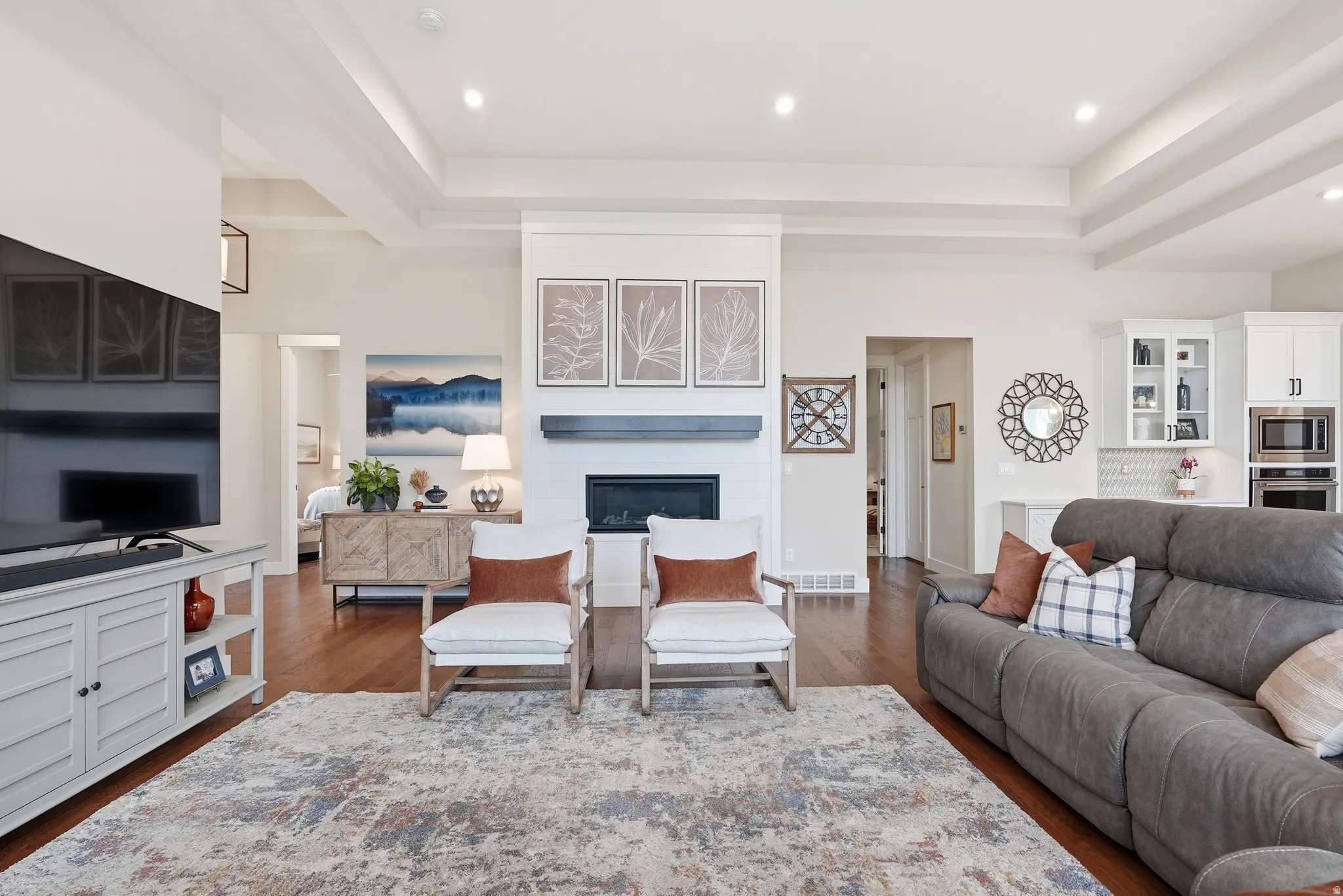 Living area with a raised ceiling, a glass covered fireplace, dark wood-style flooring, and recessed lighting