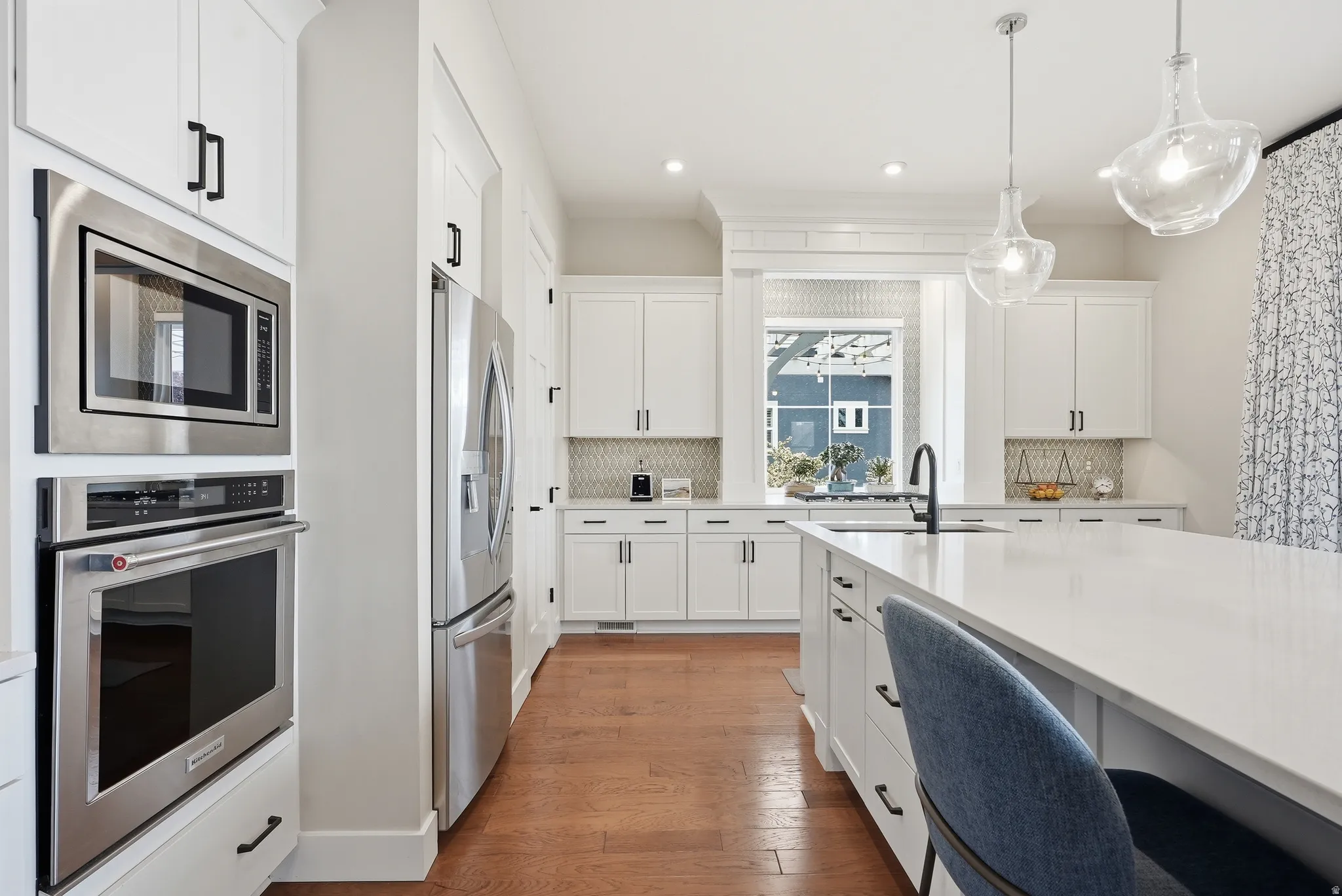 Kitchen with stainless steel appliances, white cabinetry, dark wood-style flooring, and decorative backsplash