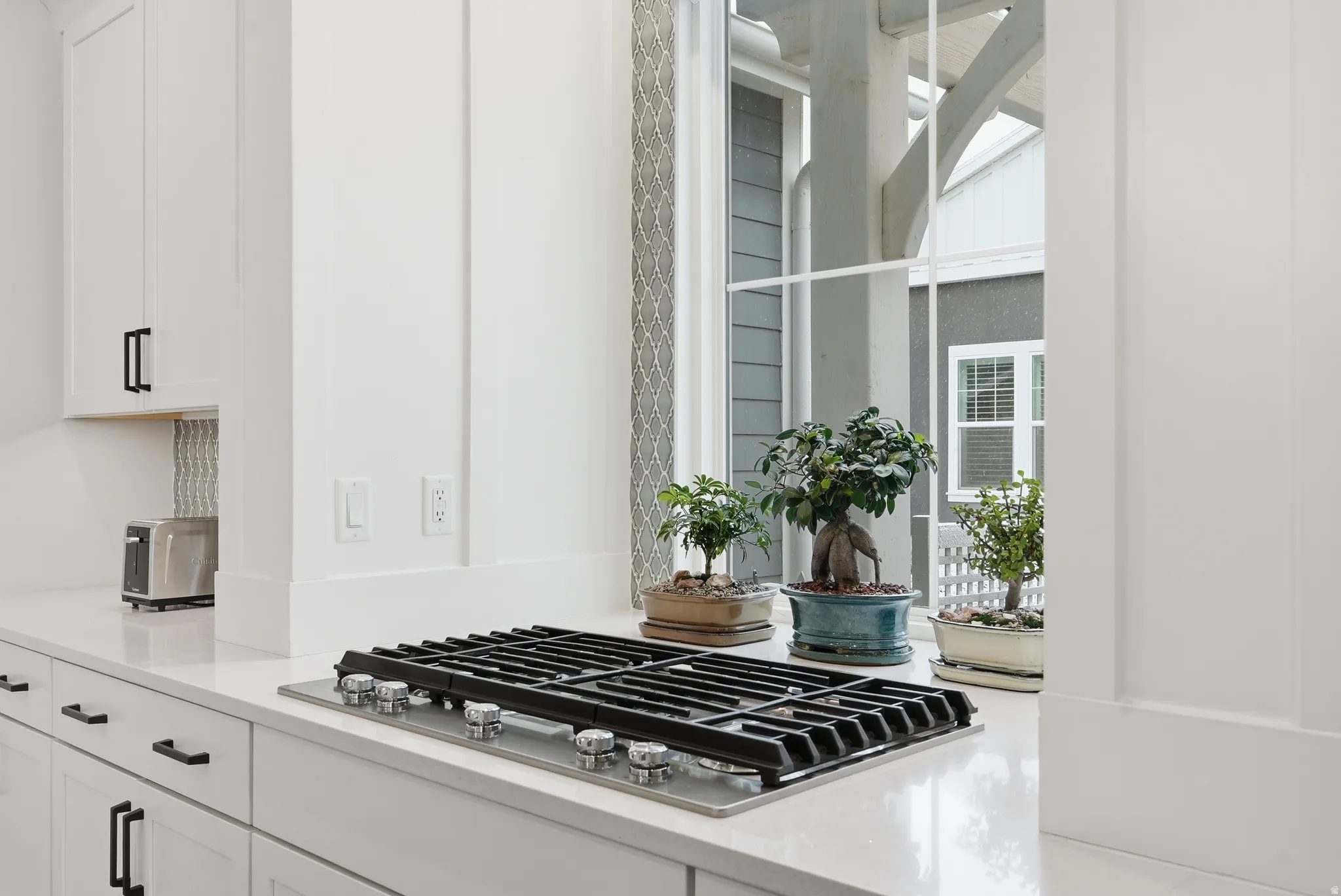 Kitchen view of white cabinets, stainless steel gas stovetop, and light stone countertops