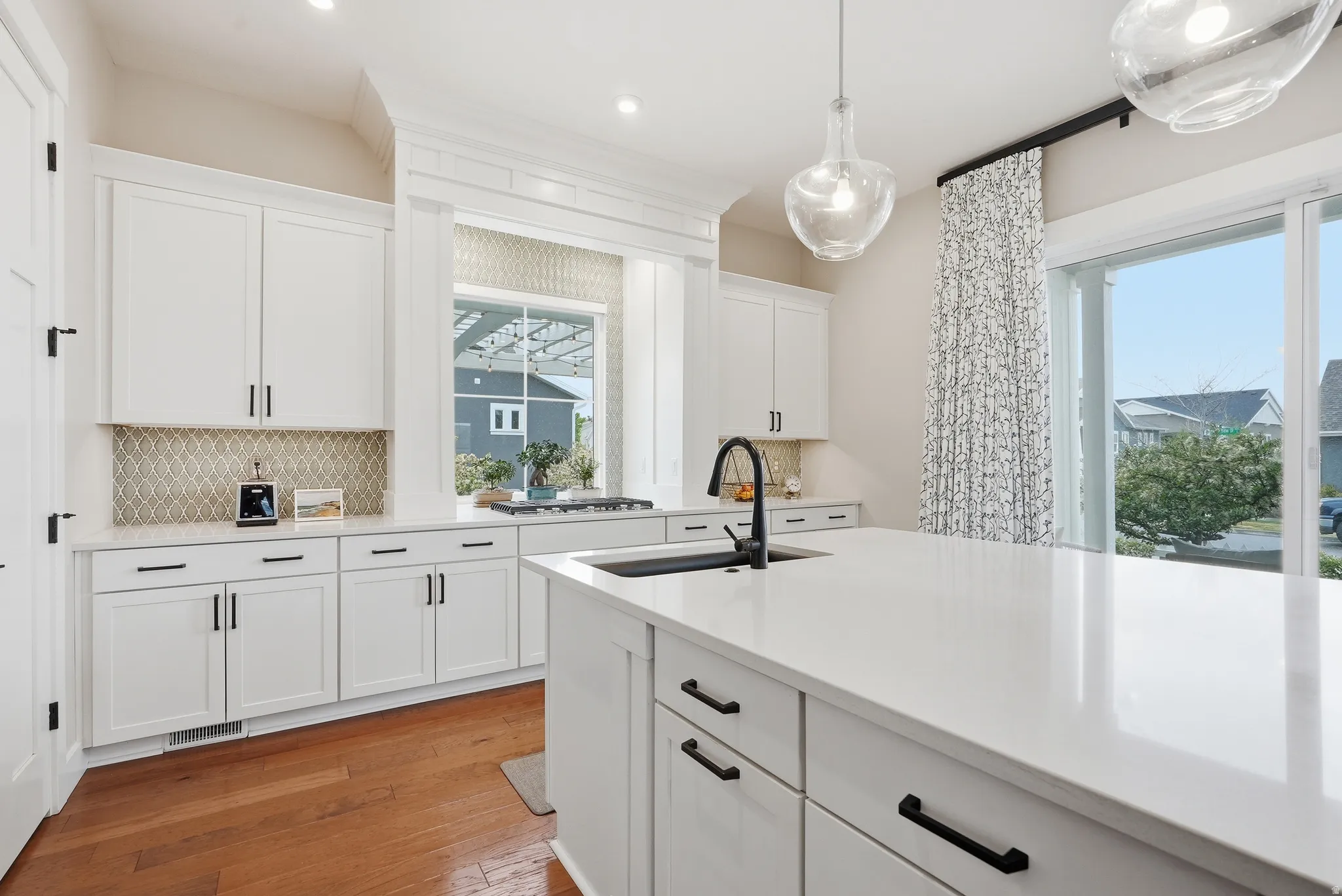 Kitchen with white cabinetry, light wood-type flooring, backsplash, light stone counters, and hanging light fixtures