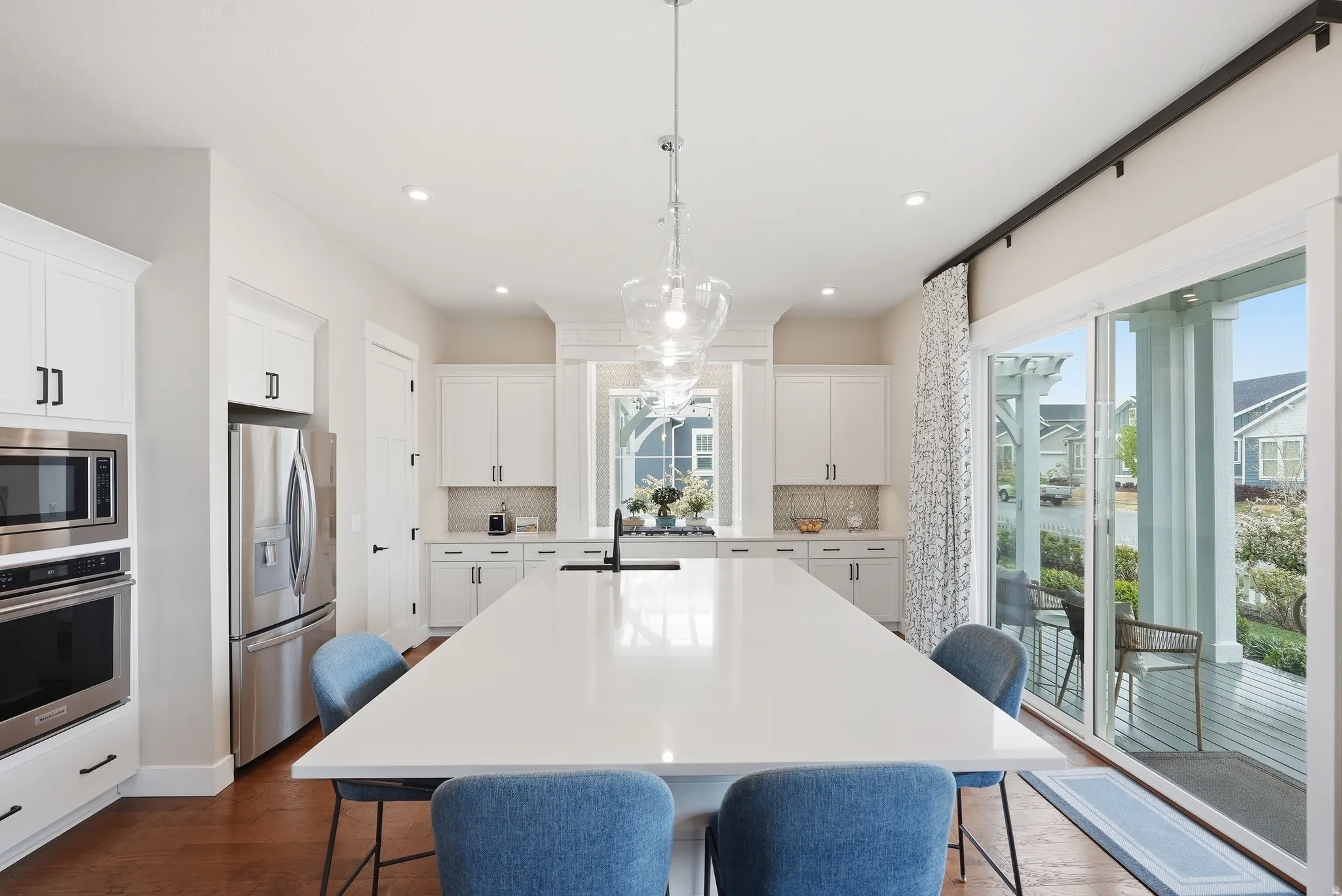 Kitchen featuring a kitchen bar, an island with sink, stainless steel appliances, white cabinetry, and hanging light fixtures
