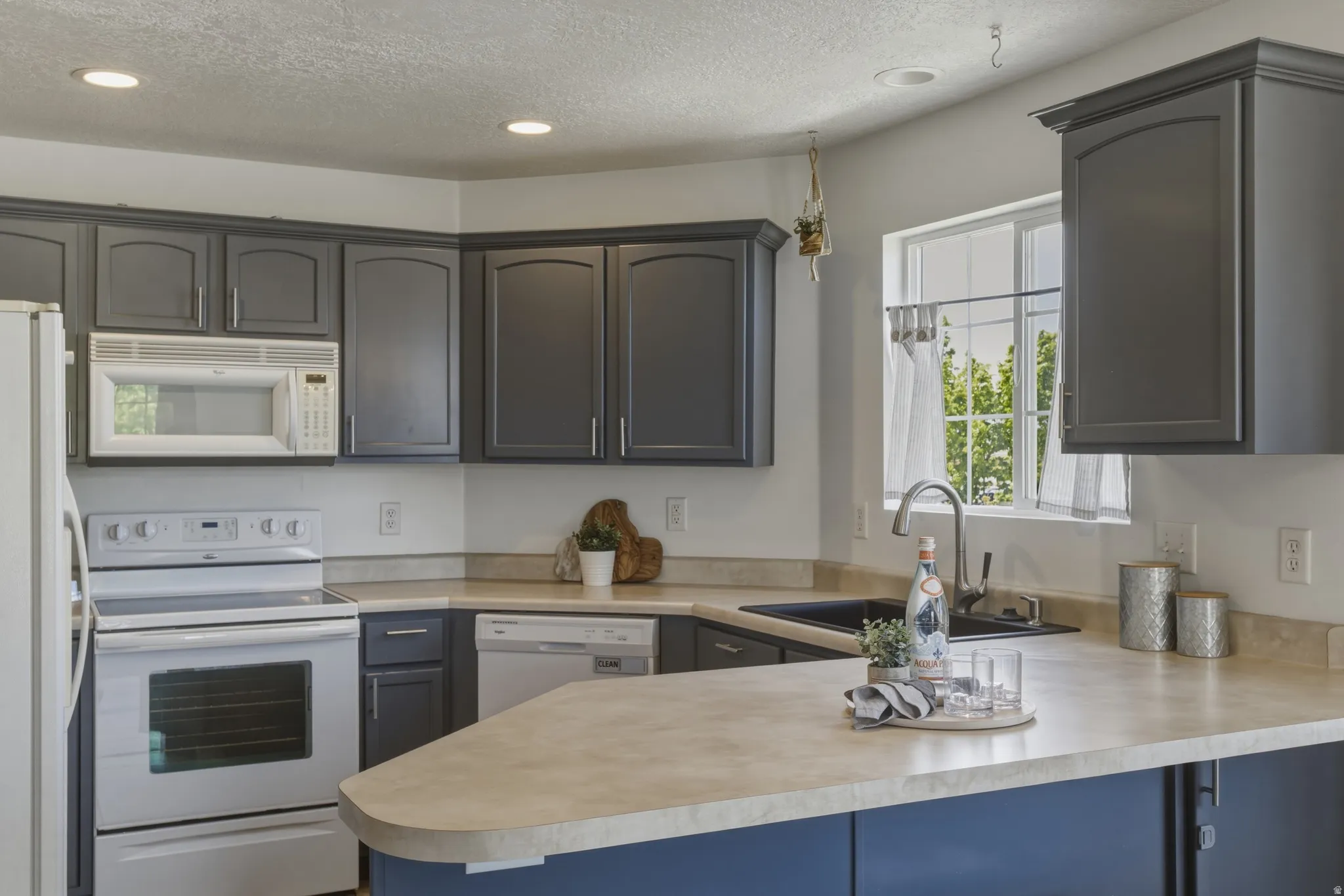Kitchen featuring white appliances, light countertops, recessed lighting, a textured ceiling, and a peninsula