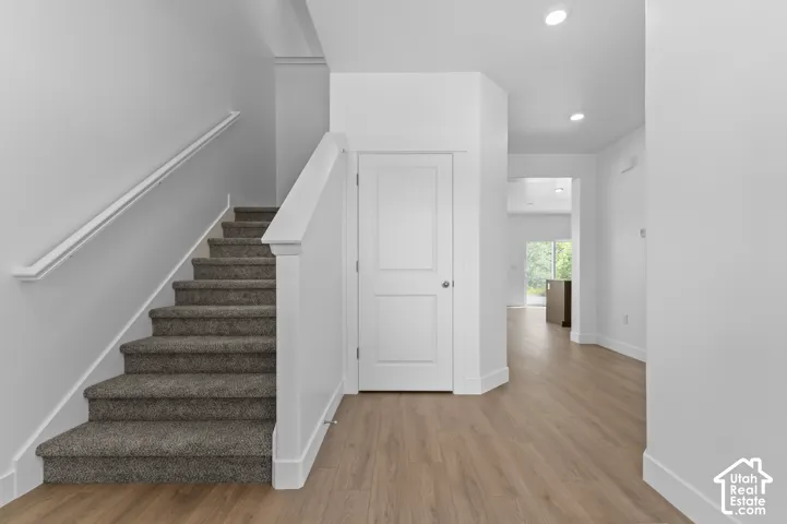 Carpeted staircase with white handrail, wood-finish flooring, and recessed ceiling lighting