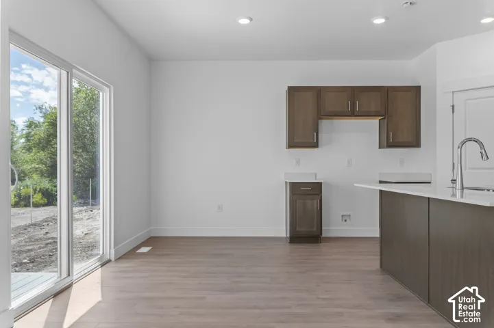 Sliding glass patio door, wood-finish flooring, recessed lighting, dark wood-finish cabinetry, and a kitchen island with a single-basin sink