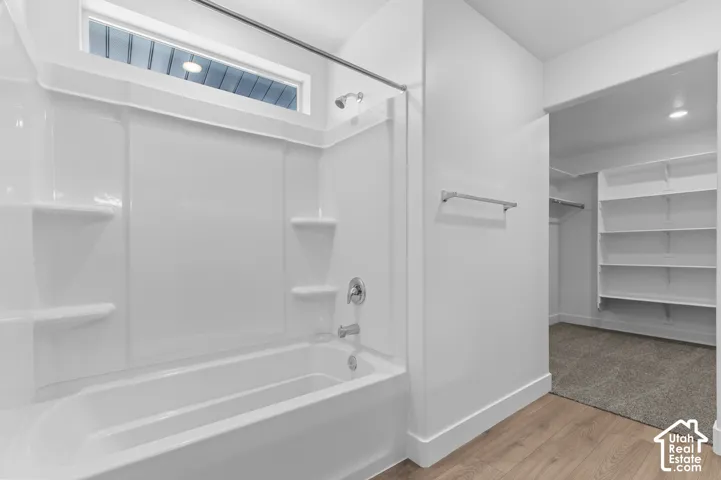 White bathtub with shower, integrated shelving, and an upper transom window