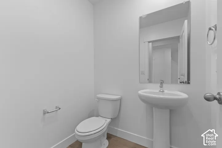 Pedestal sink with chrome faucet, wall-mounted mirror, white toilet, and wood-finish flooring