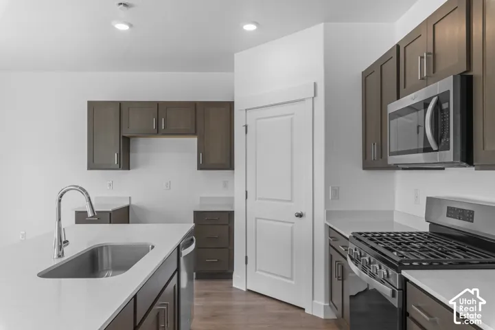 Kitchen featuring a stainless steel sink with gooseneck faucet, light-toned countertops, wood-finish cabinetry, a stainless steel microwave, and a gas range