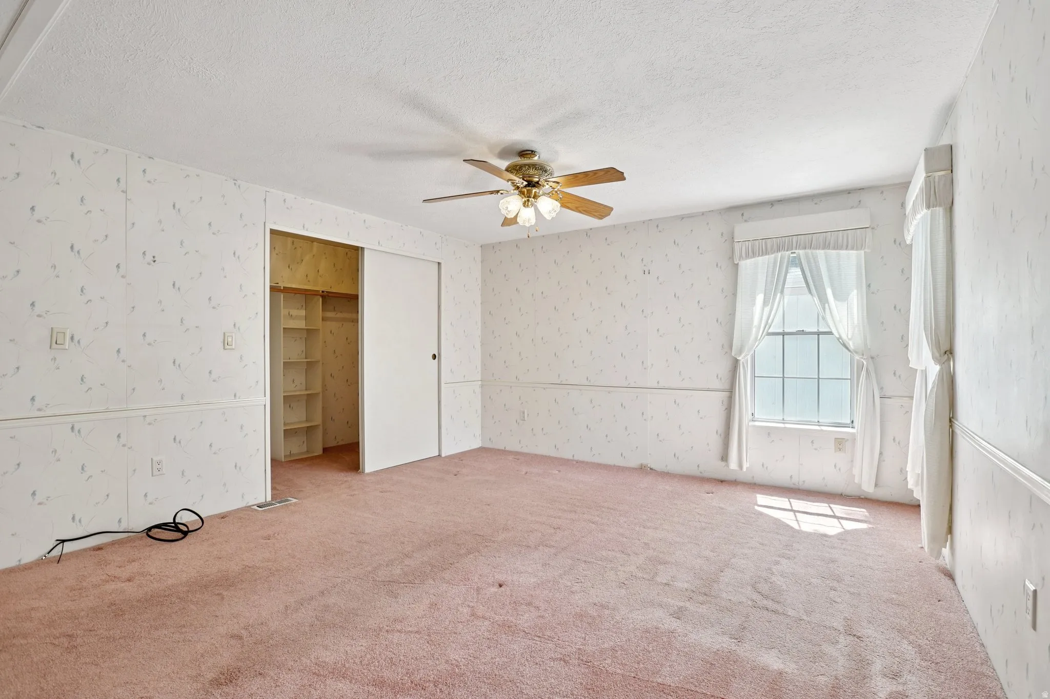 Unfurnished bedroom with carpet, ceiling fan, a textured ceiling, wallpapered walls, and a closet