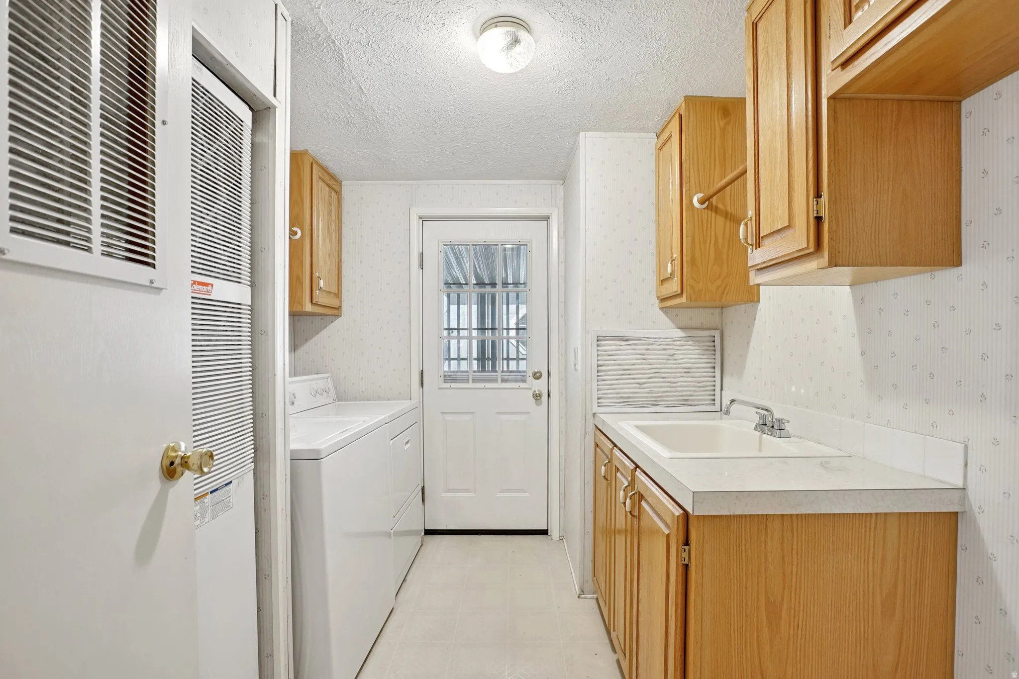 Laundry room featuring a textured ceiling, light floors, cabinet space, a heating unit, and washing machine and clothes dryer