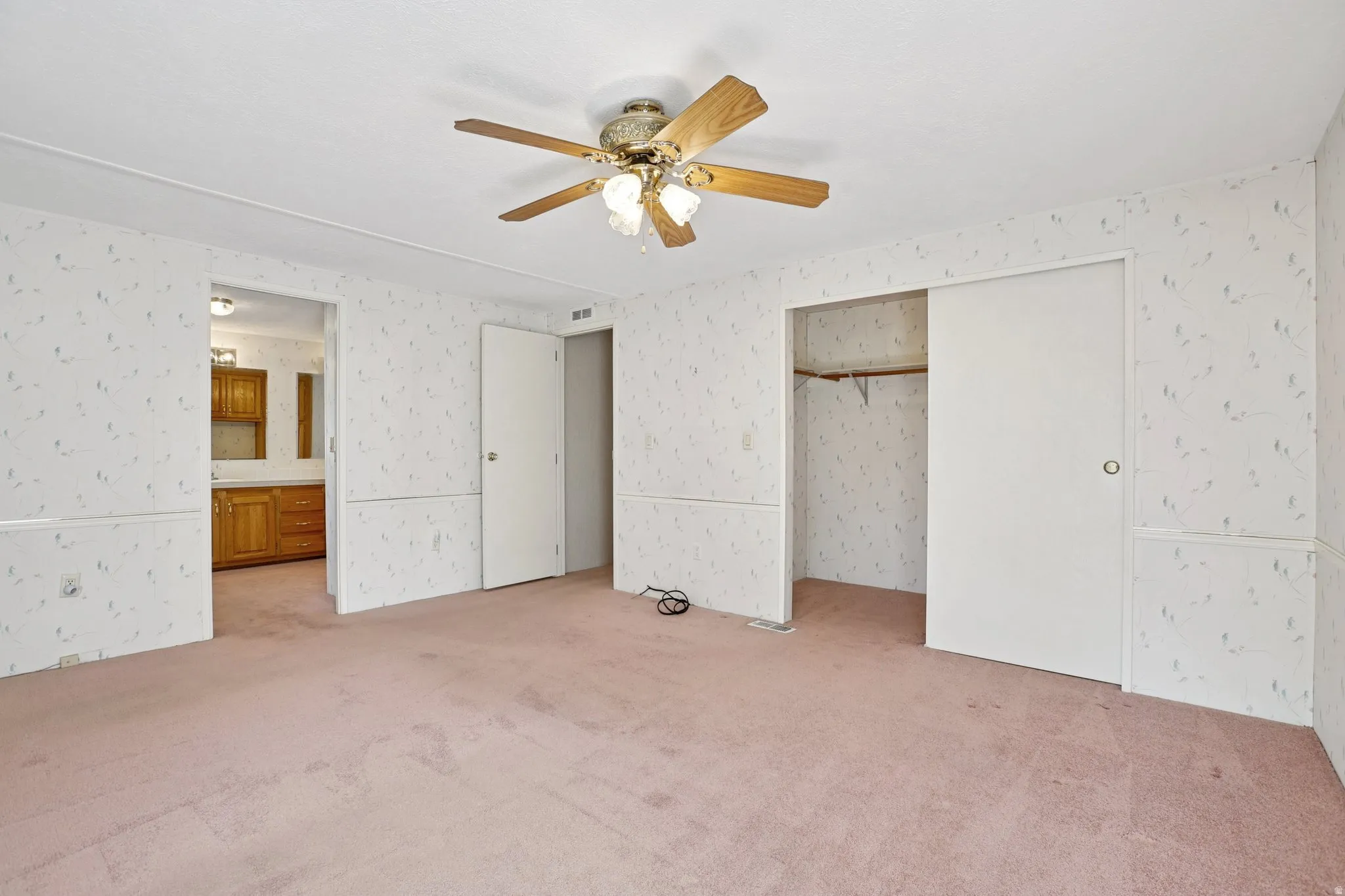 Unfurnished bedroom featuring carpet floors, a ceiling fan, a closet, ensuite bathroom, and wallpapered walls
