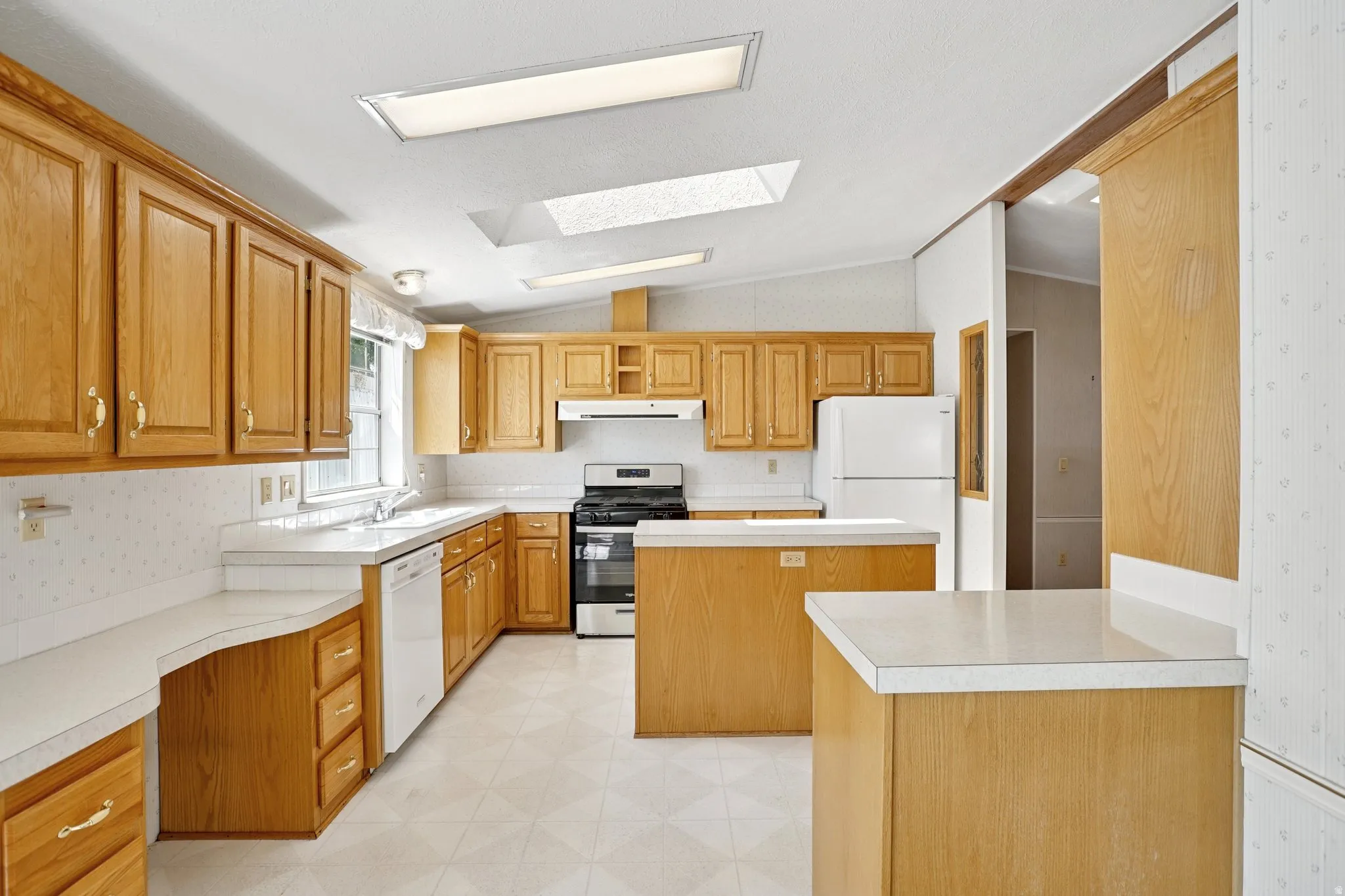 Kitchen featuring light floors, white appliances, lofted ceiling, light countertops, and wood finish cabinets