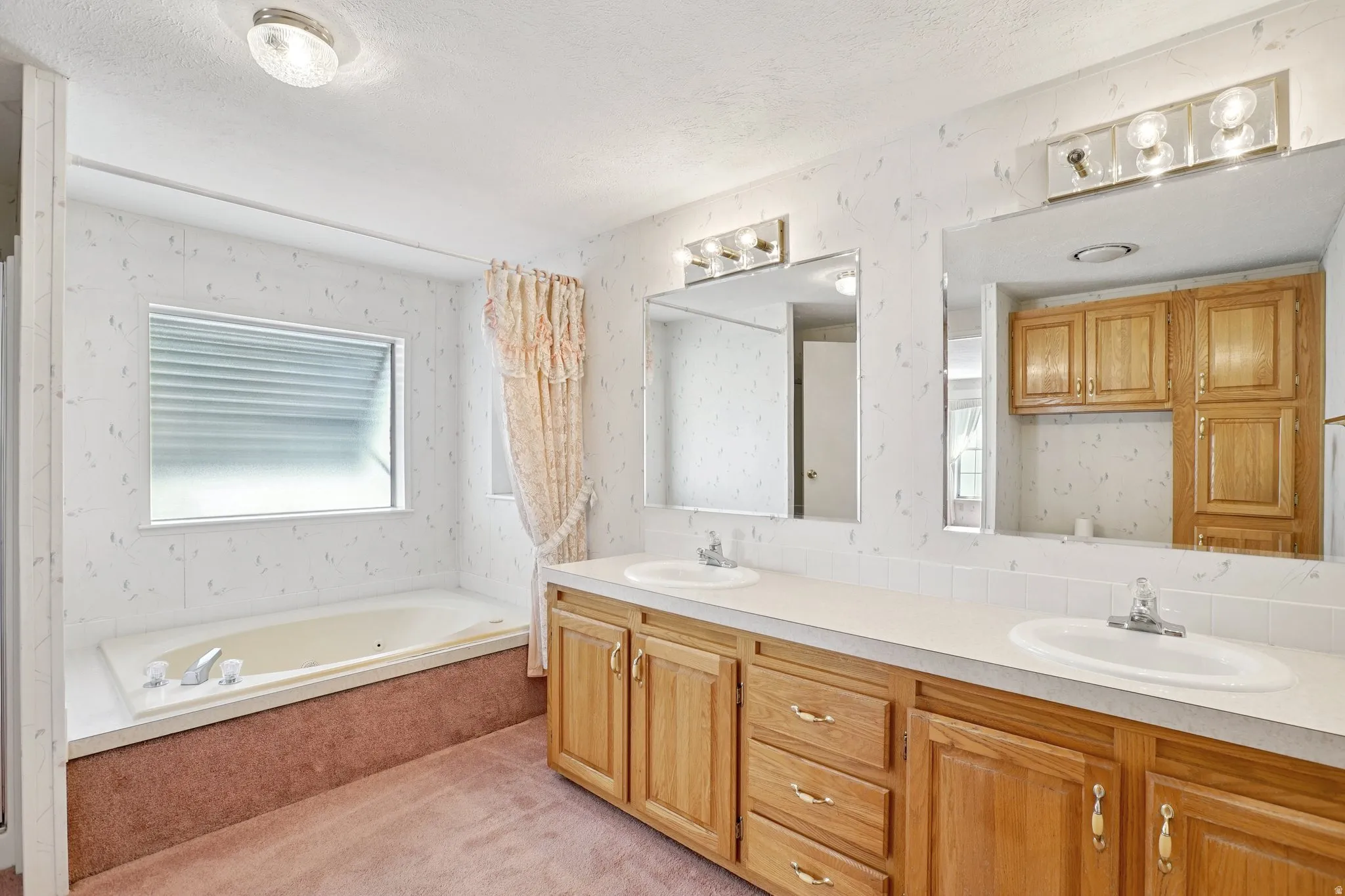 Bathroom with double vanity, a bath, wallpapered walls, and a textured ceiling