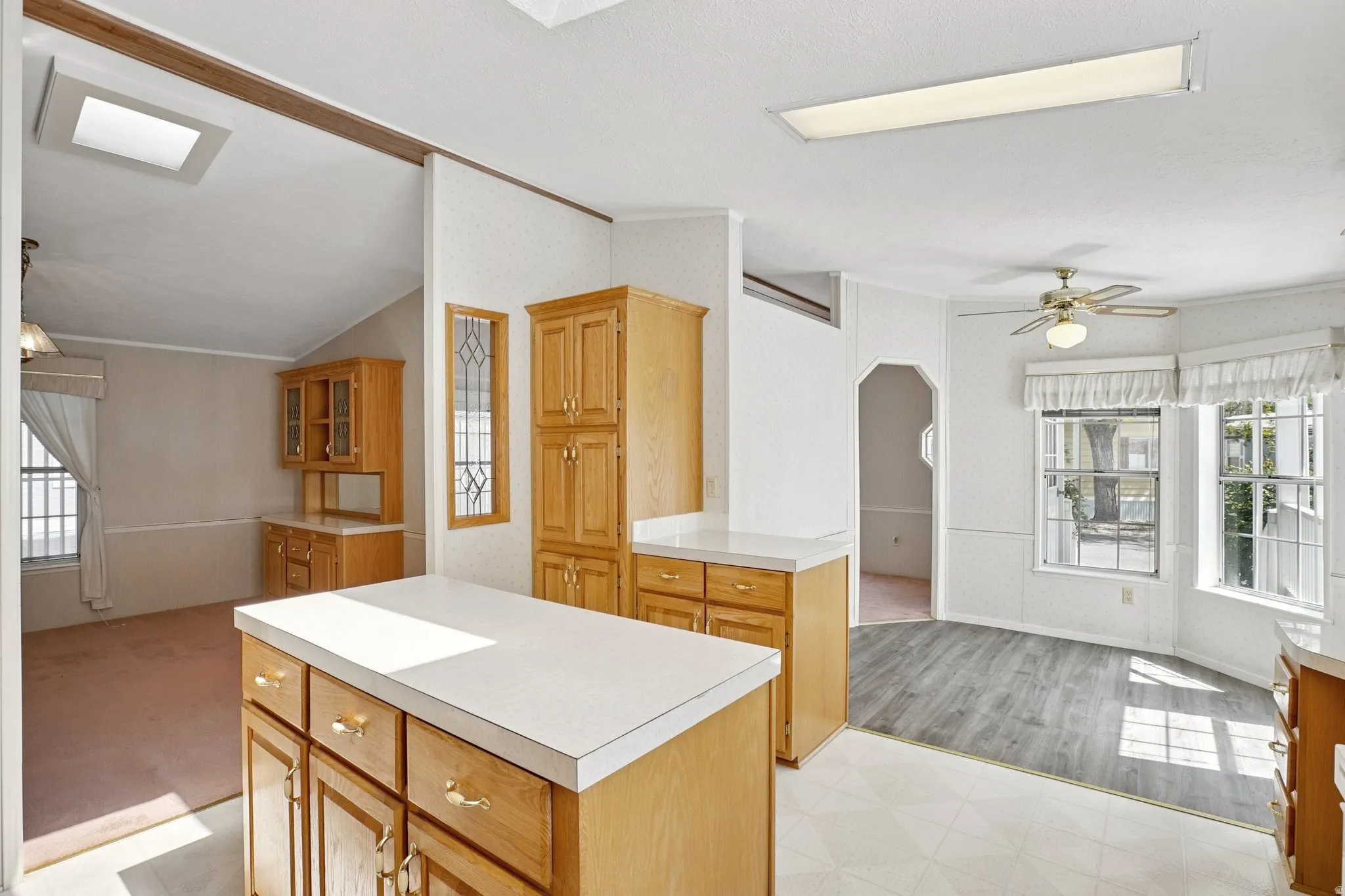 Kitchen featuring a ceiling fan, light countertops, open floor plan, crown molding, and a kitchen island