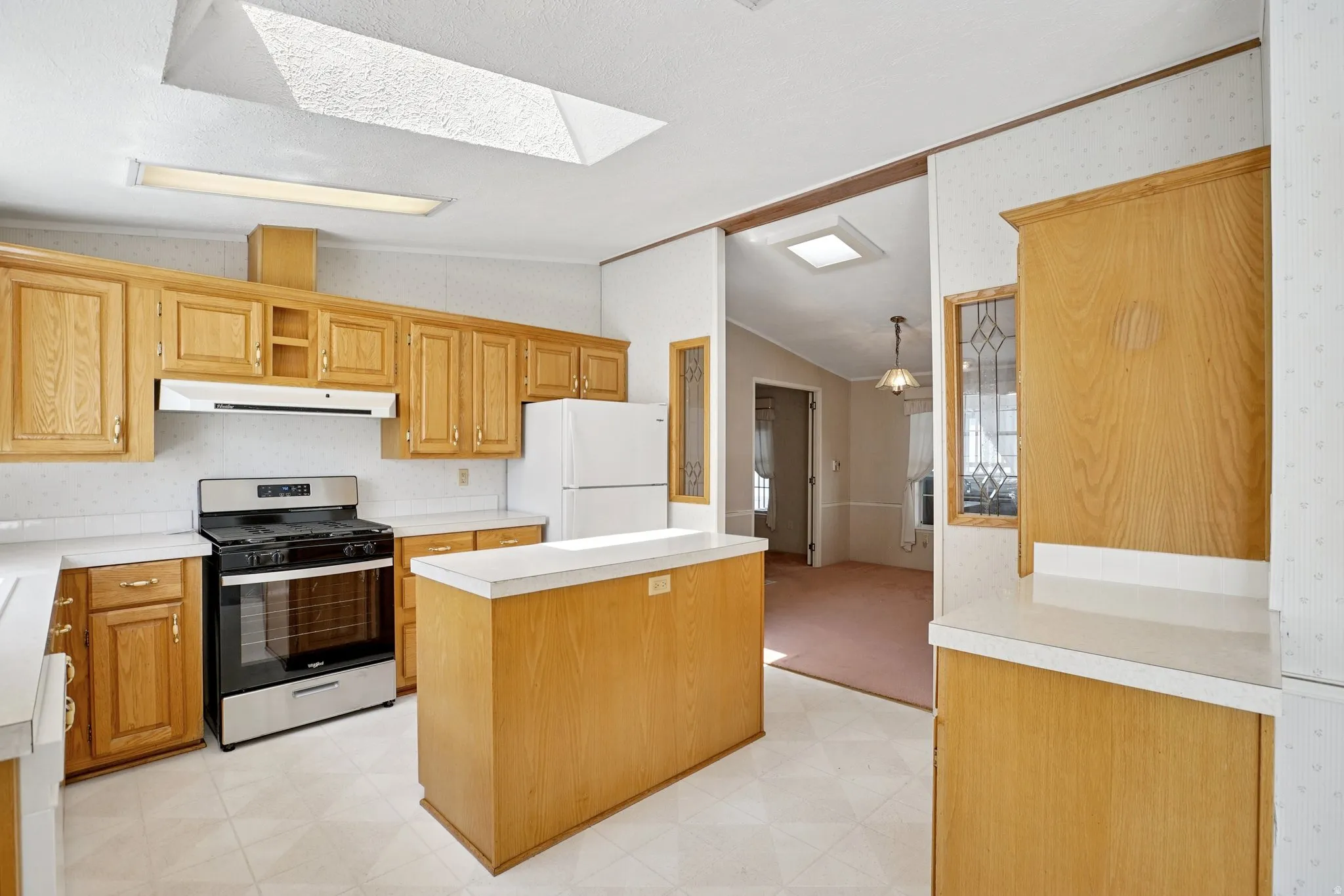 Kitchen with light flooring, gas stove, light countertops, lofted ceiling, and wallpapered walls