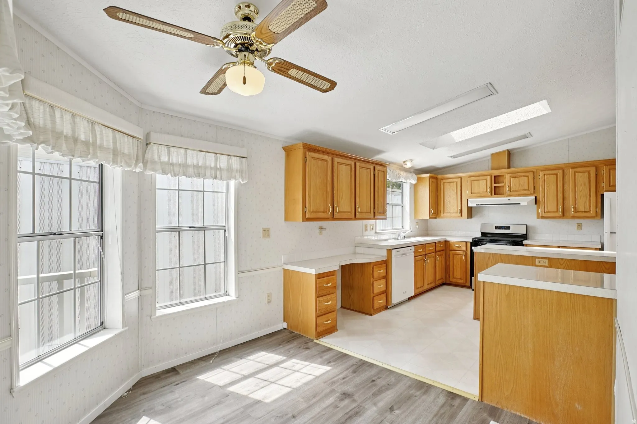Kitchen featuring light countertops, vaulted ceiling, dishwasher, ceiling fan, and wood finish cabinets