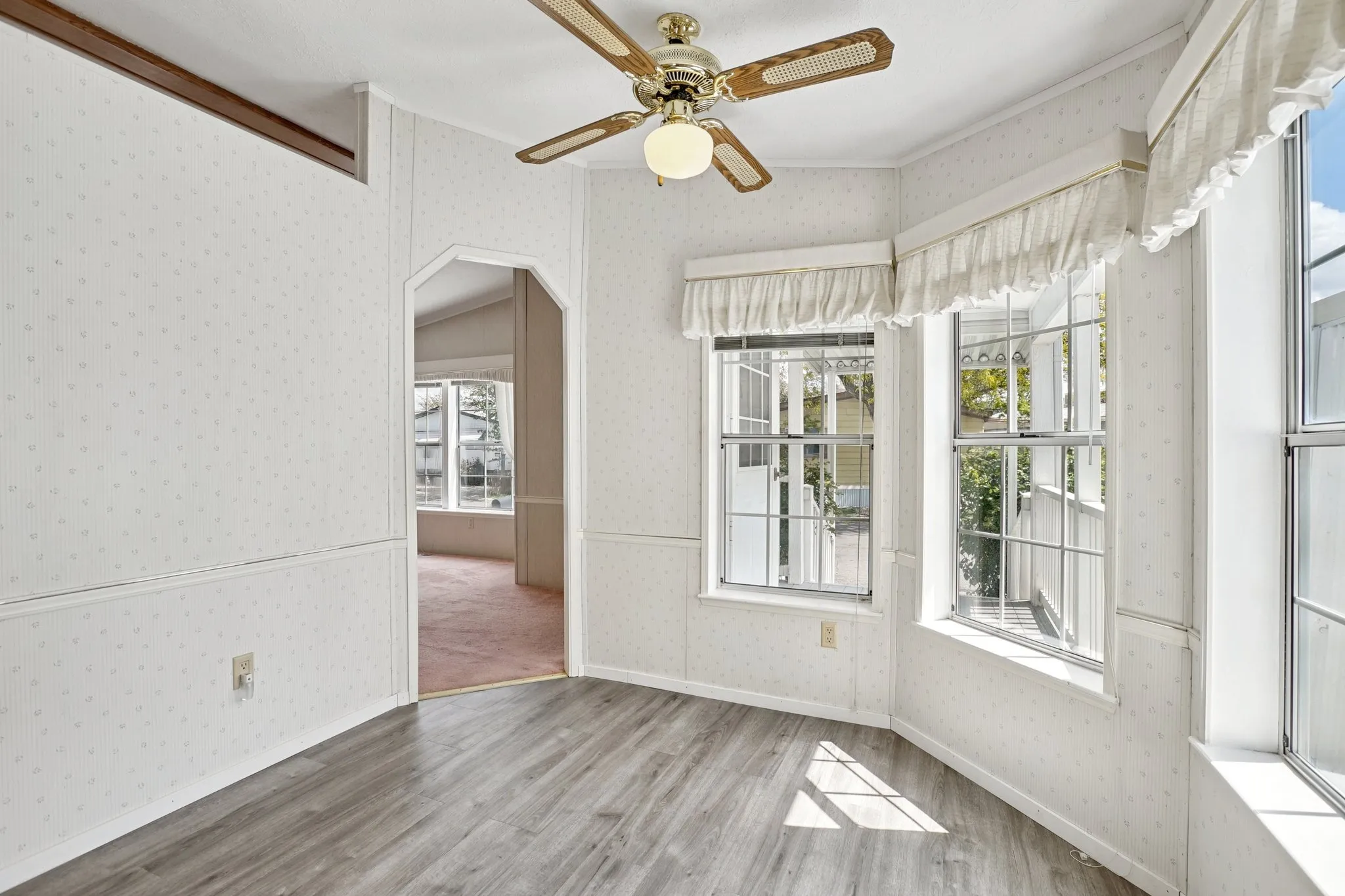 Spare room with wallpapered walls, a ceiling fan, wood finished floors, and arched walkways
