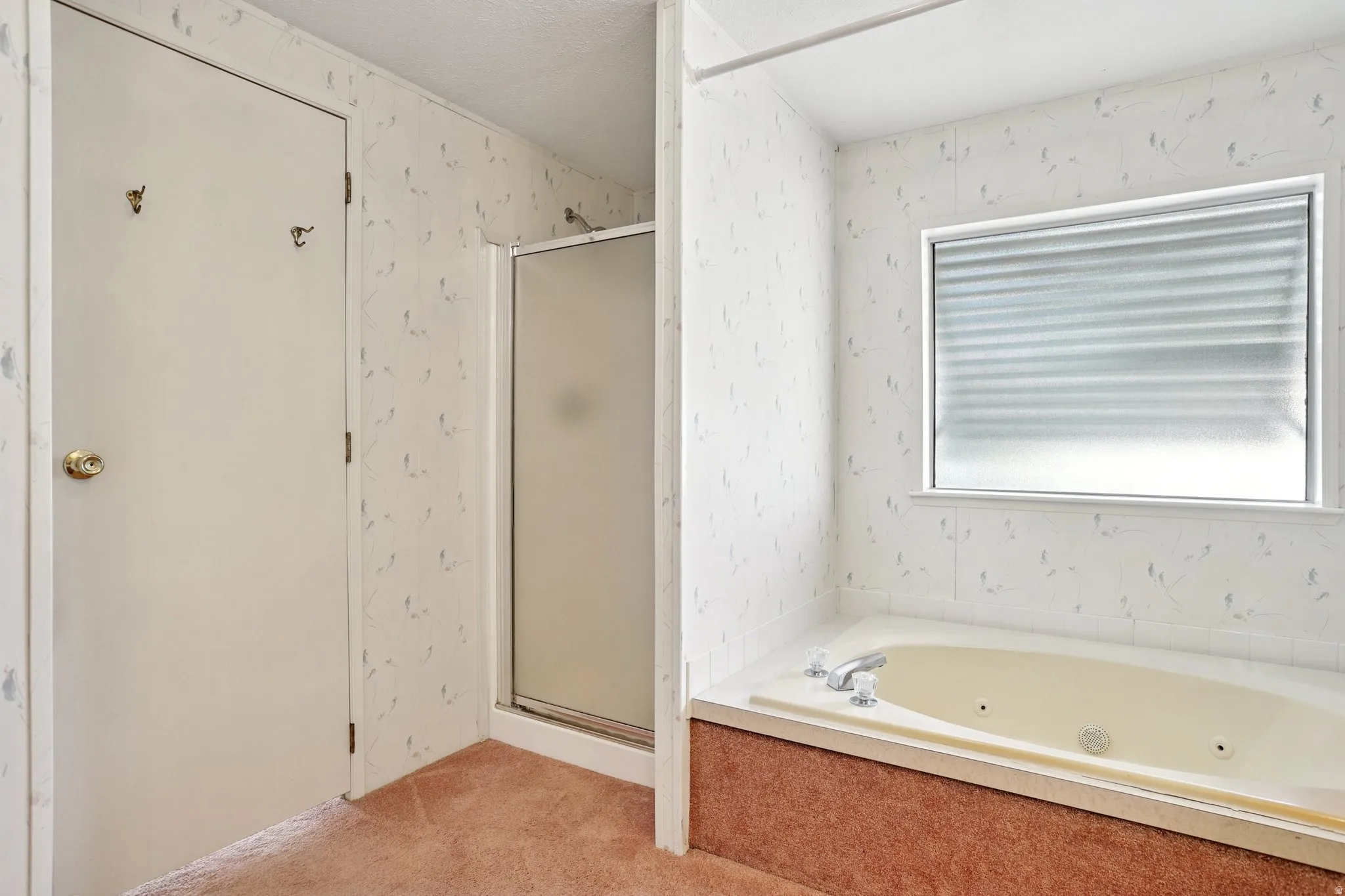 Bathroom with a stall shower, wallpapered walls, light colored carpet, a tub with jets, and a textured ceiling
