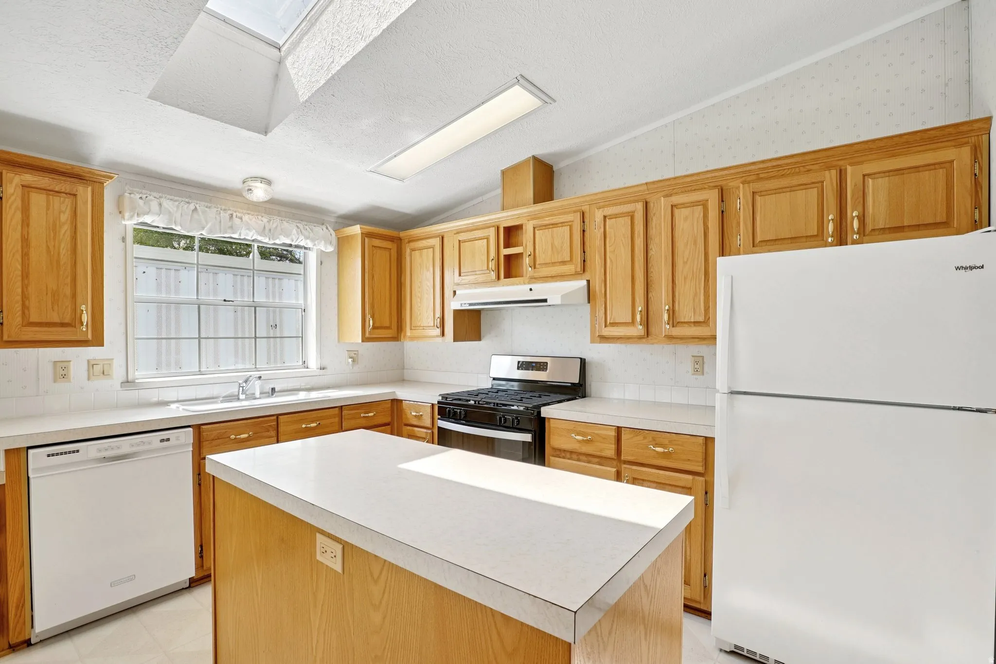 Kitchen with white appliances, lofted ceiling, a kitchen island, light countertops, and a skylight